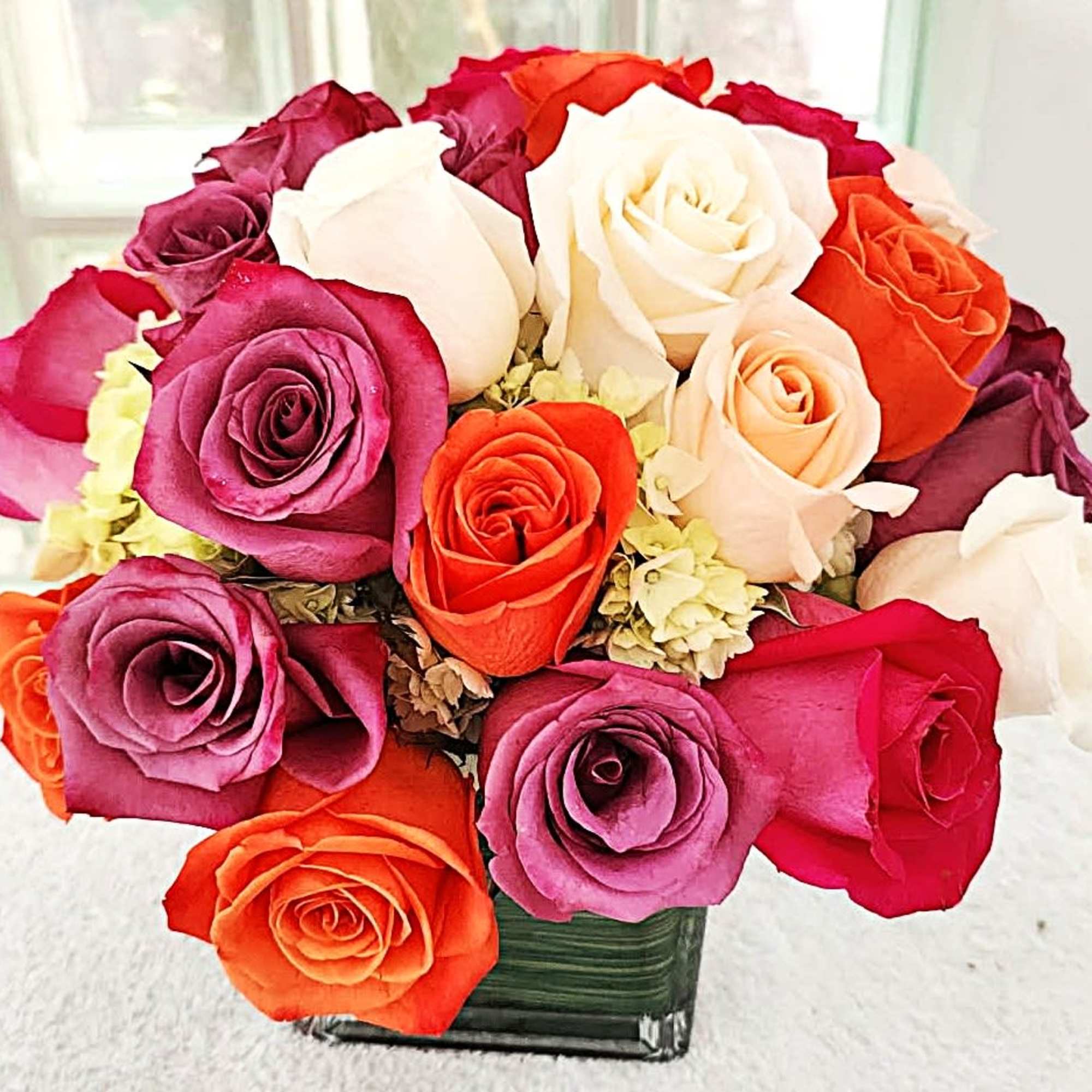 Pink, yellow and orange roses come together with green hydrangea for a