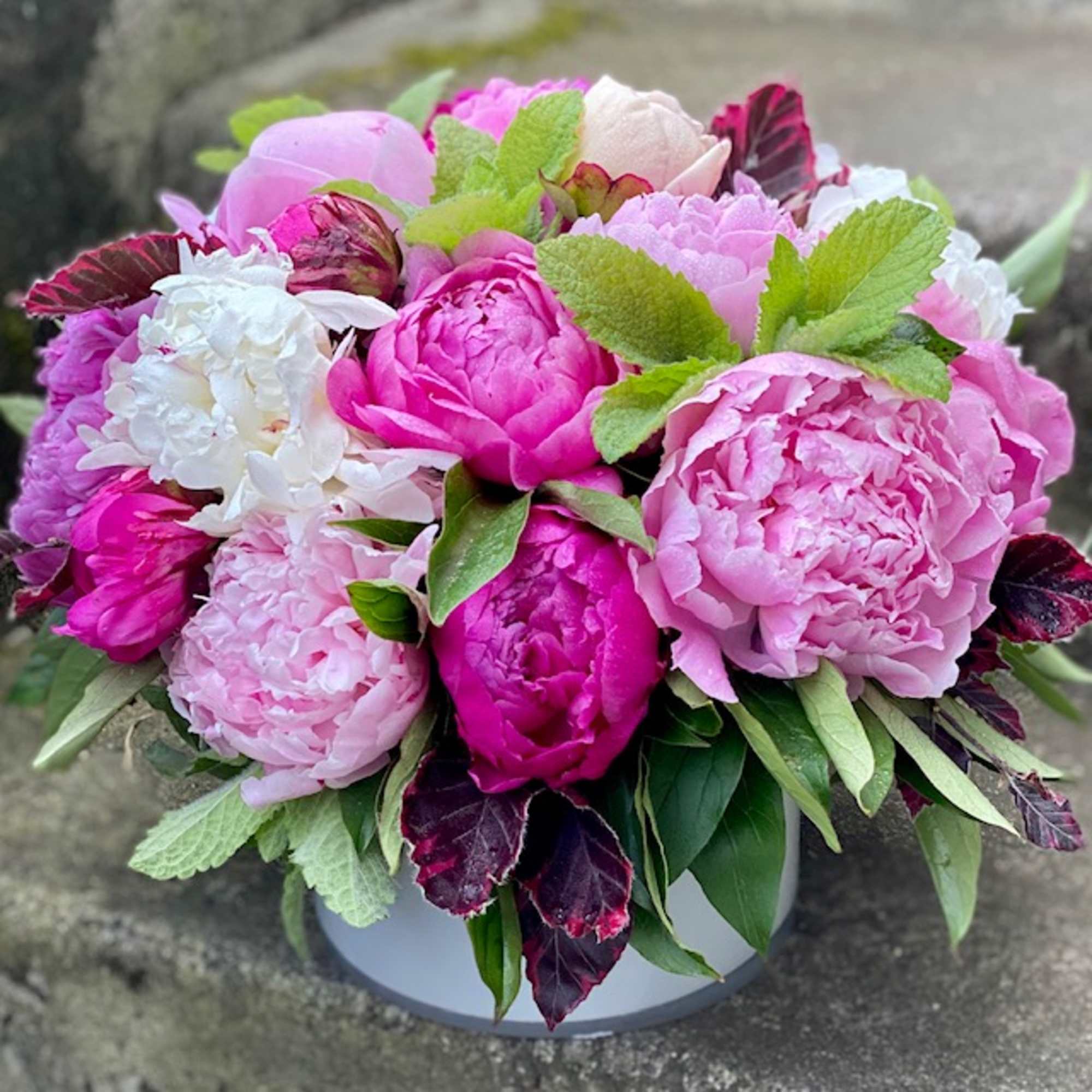 Pink peonies and white blooms arranged in a low round container
