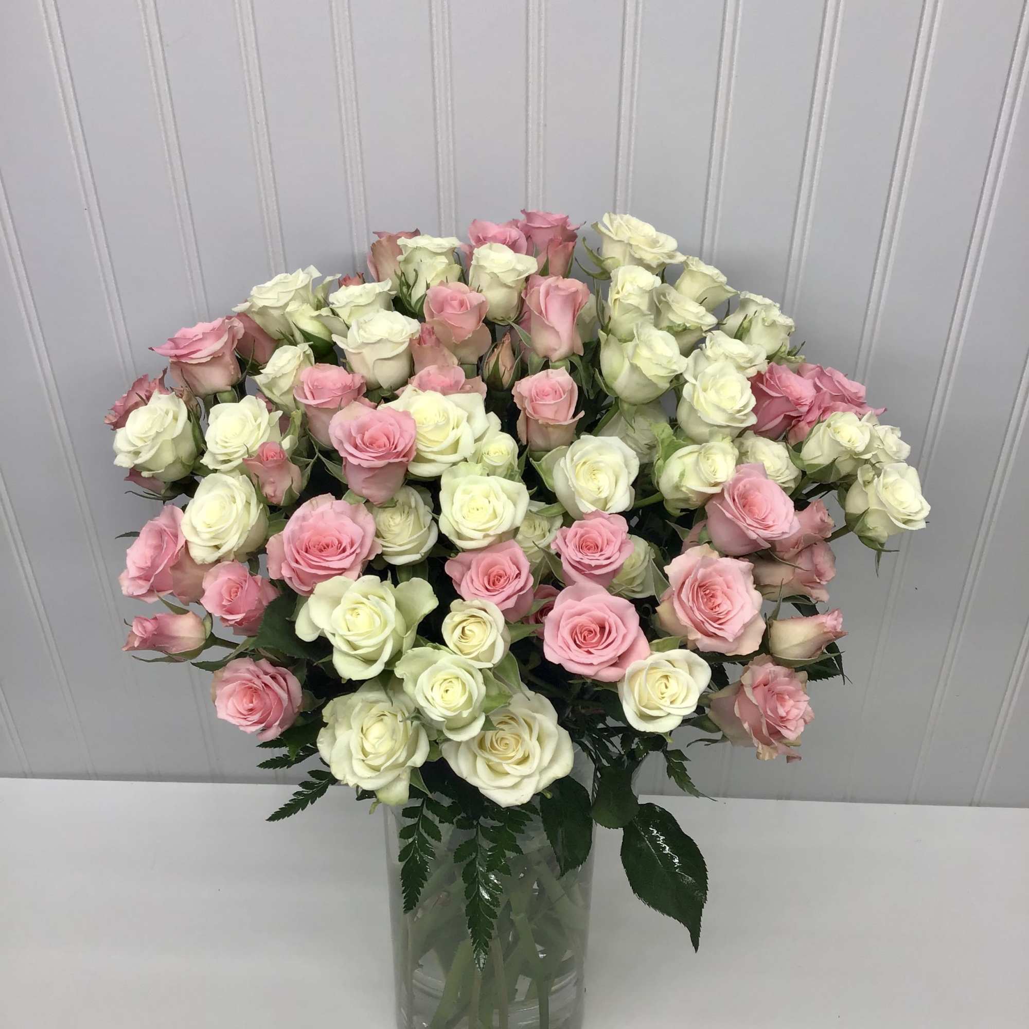 Tall glass vase filled with many pink and cream roses in a full rounded arrangement