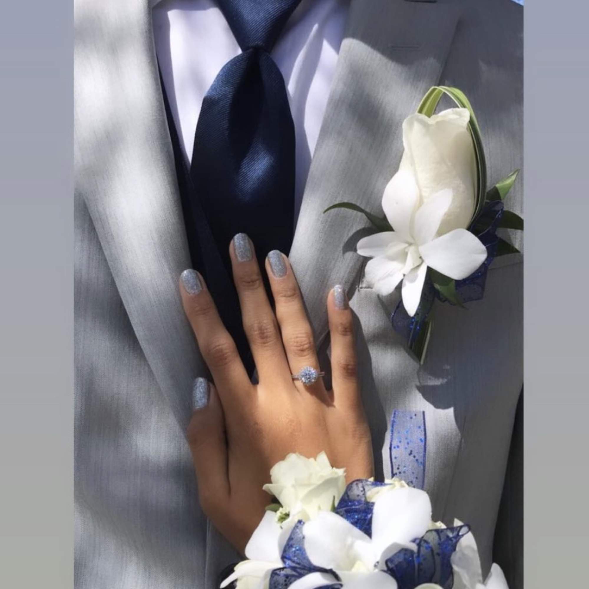 White floral corsage and boutonniere on a gray suit with a navy tie