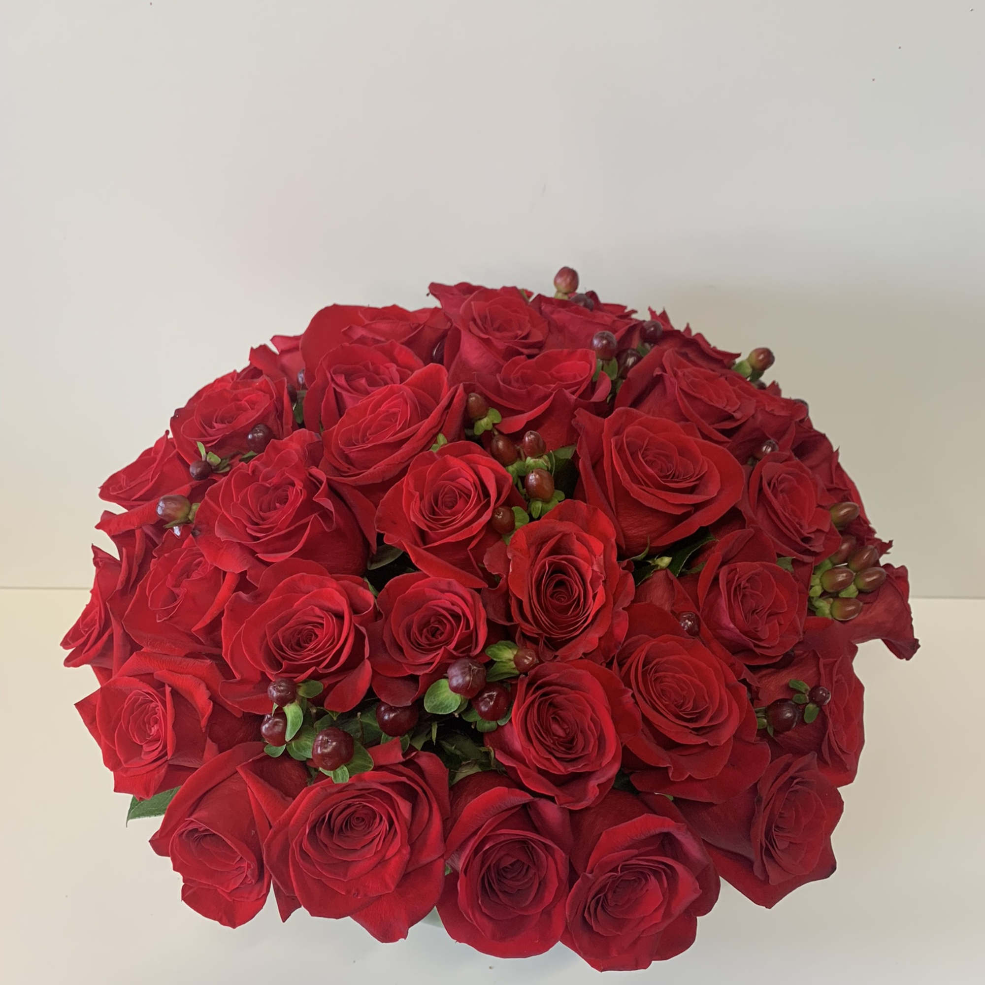Low round arrangement of tightly clustered red roses with small red berries.