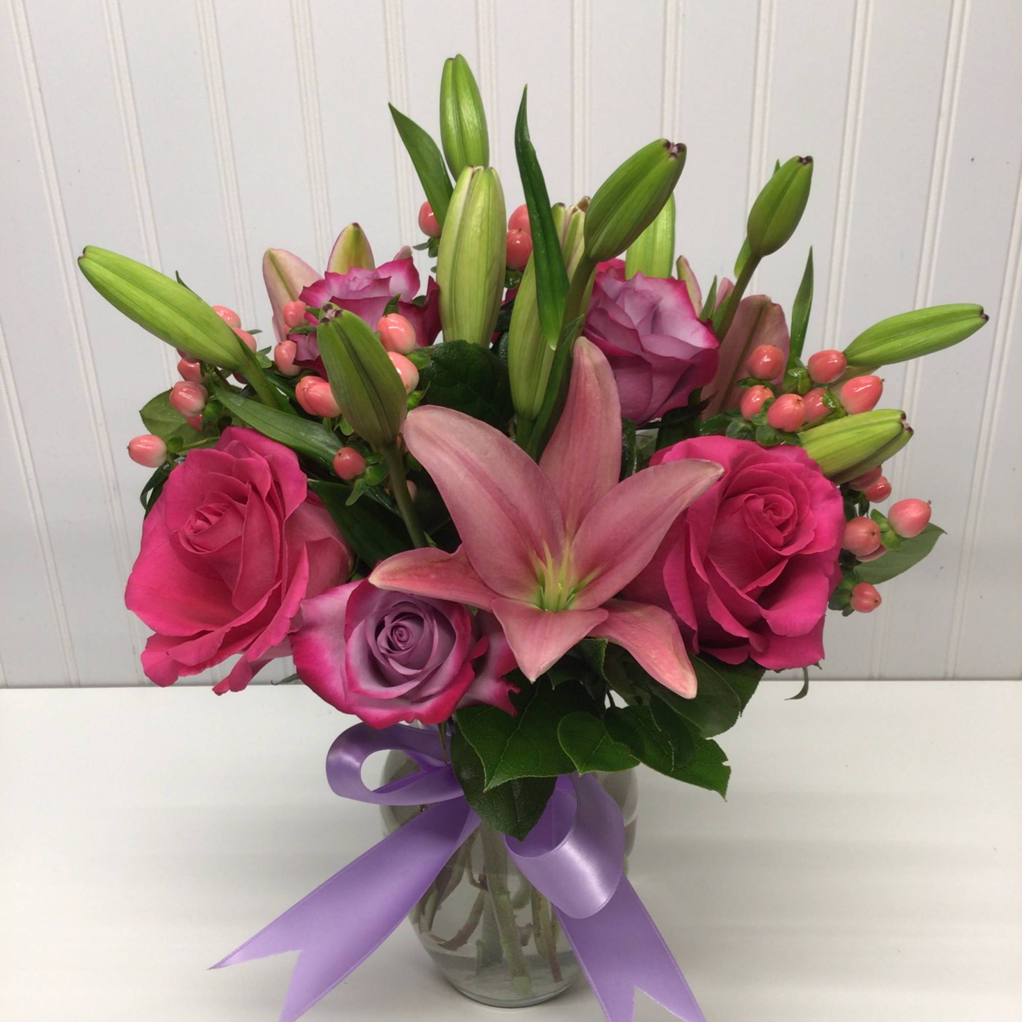 Pink lilies and roses with lavender roses in a glass vase tied with a lavender ribbon