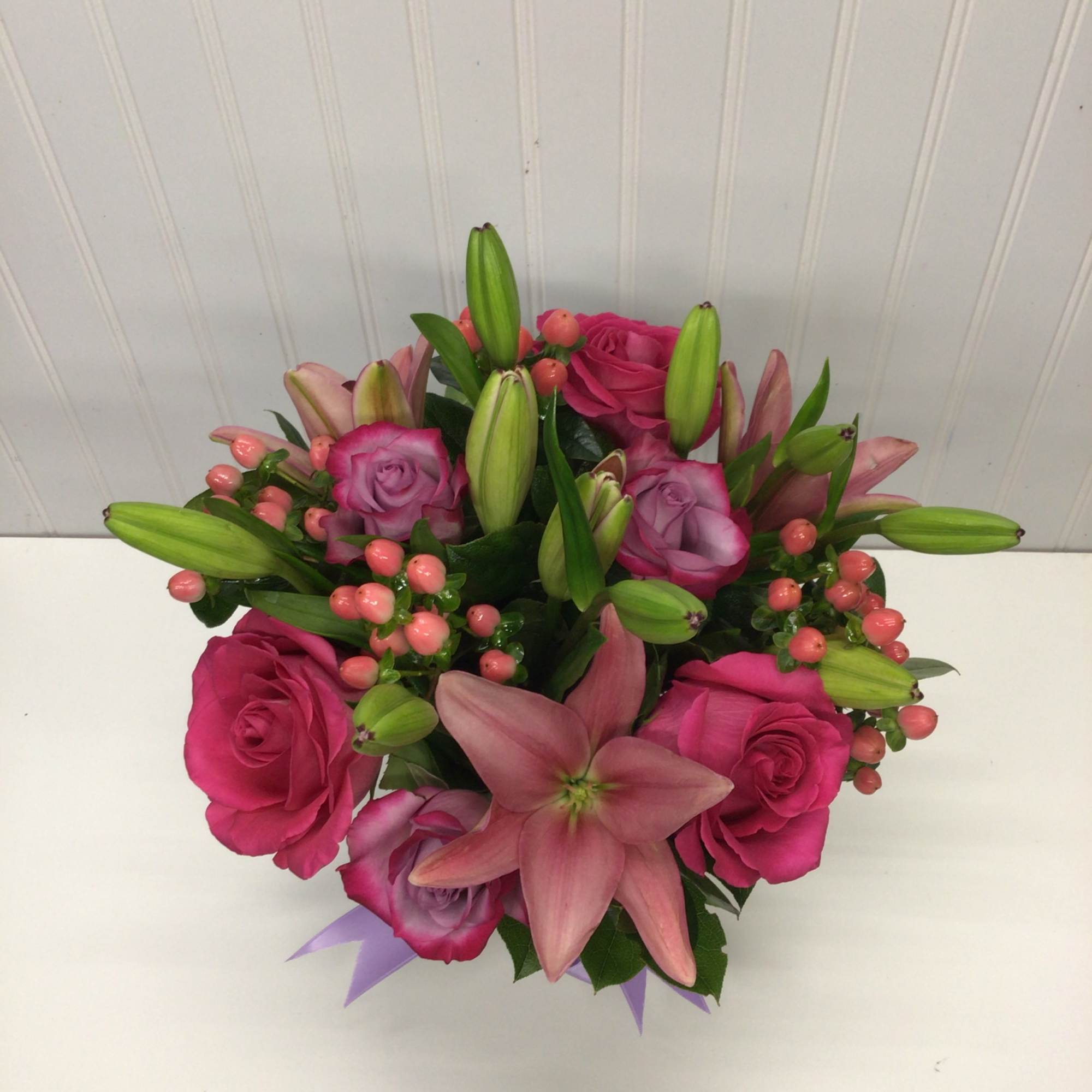 Round arrangement of pink lilies, pink and lavender roses with pink berries in a compact design