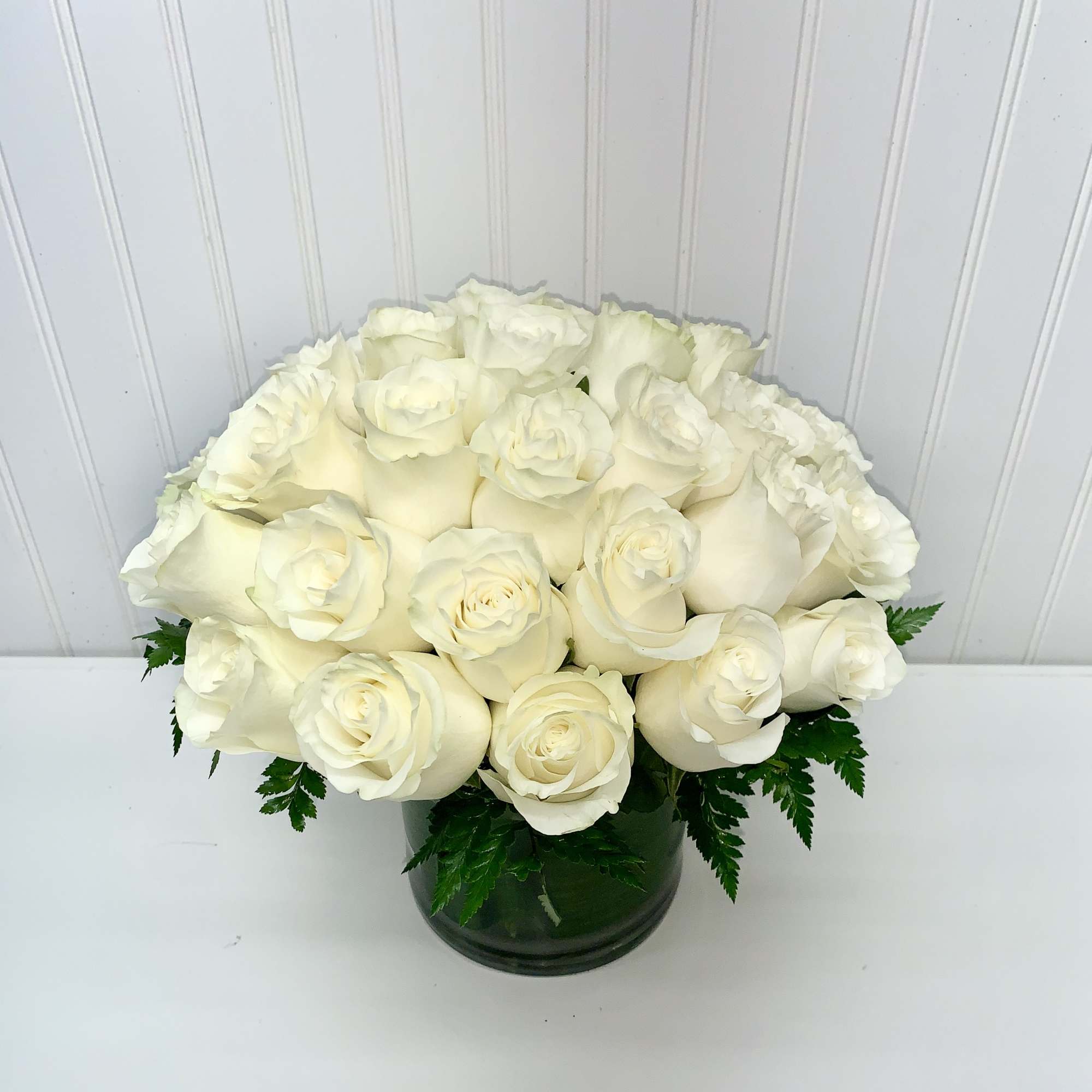 Low round arrangement of creamy white roses clustered in a clear glass cylinder vase