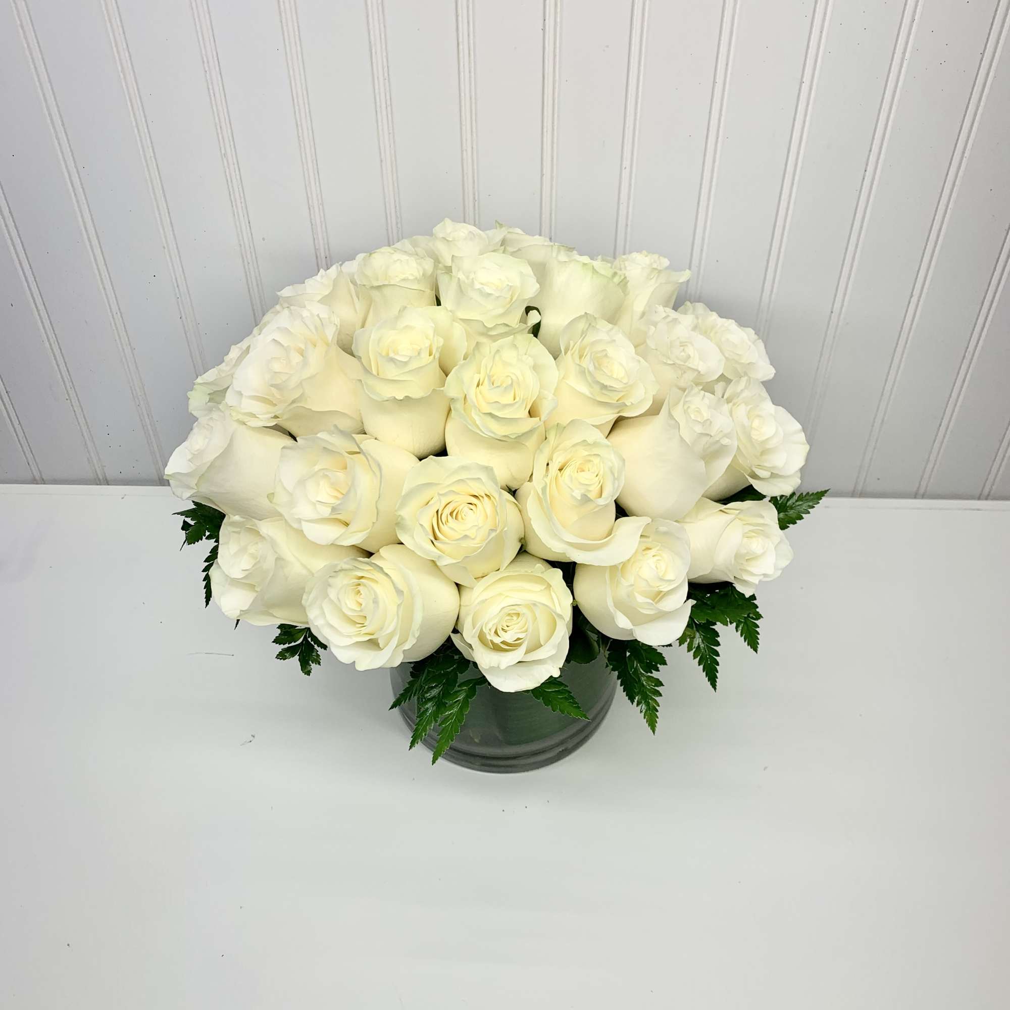 Low dome of white roses arranged tightly in a clear glass cylinder vase