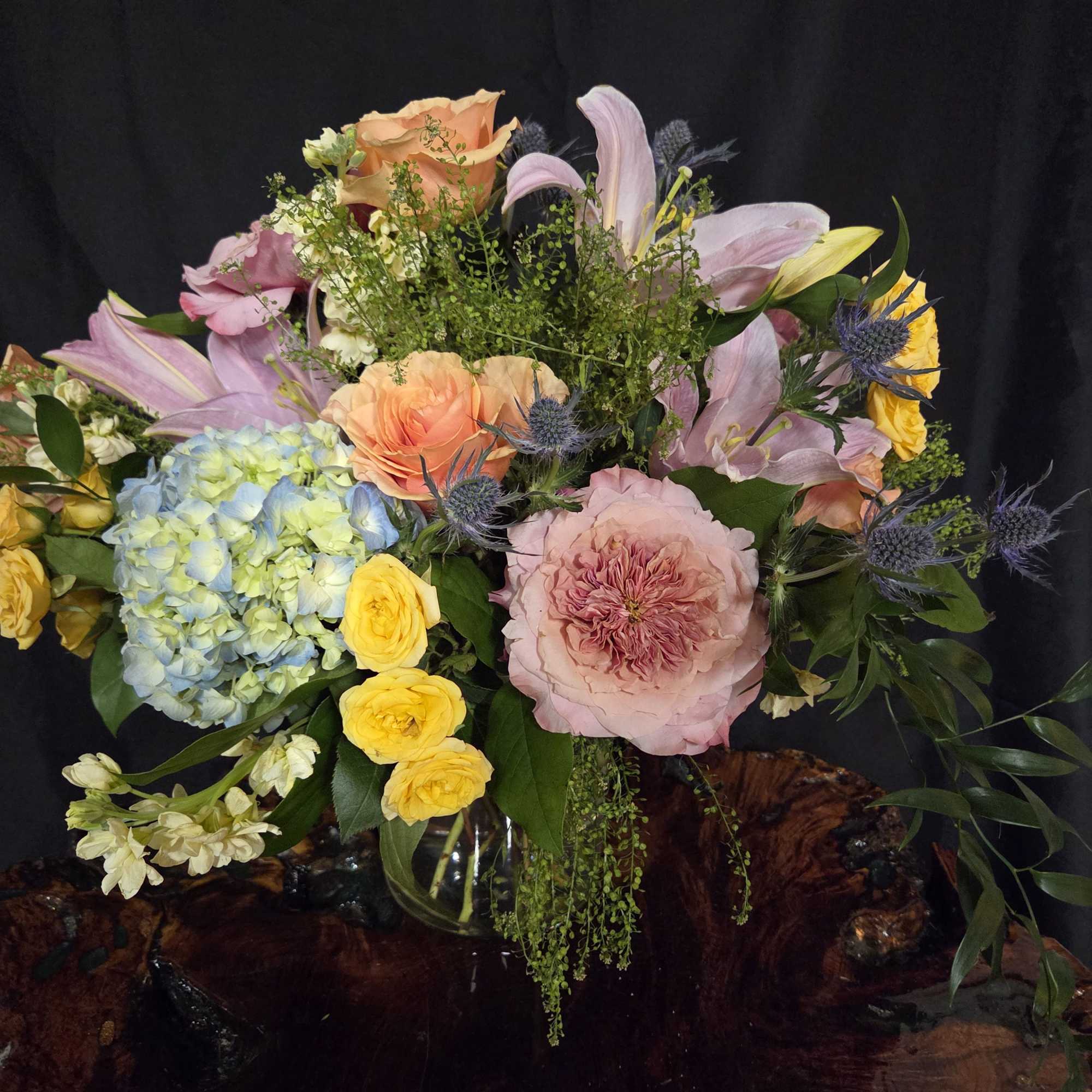 A lush, garden-inspired arrangement overflowing with soft peach and blush blooms, blue