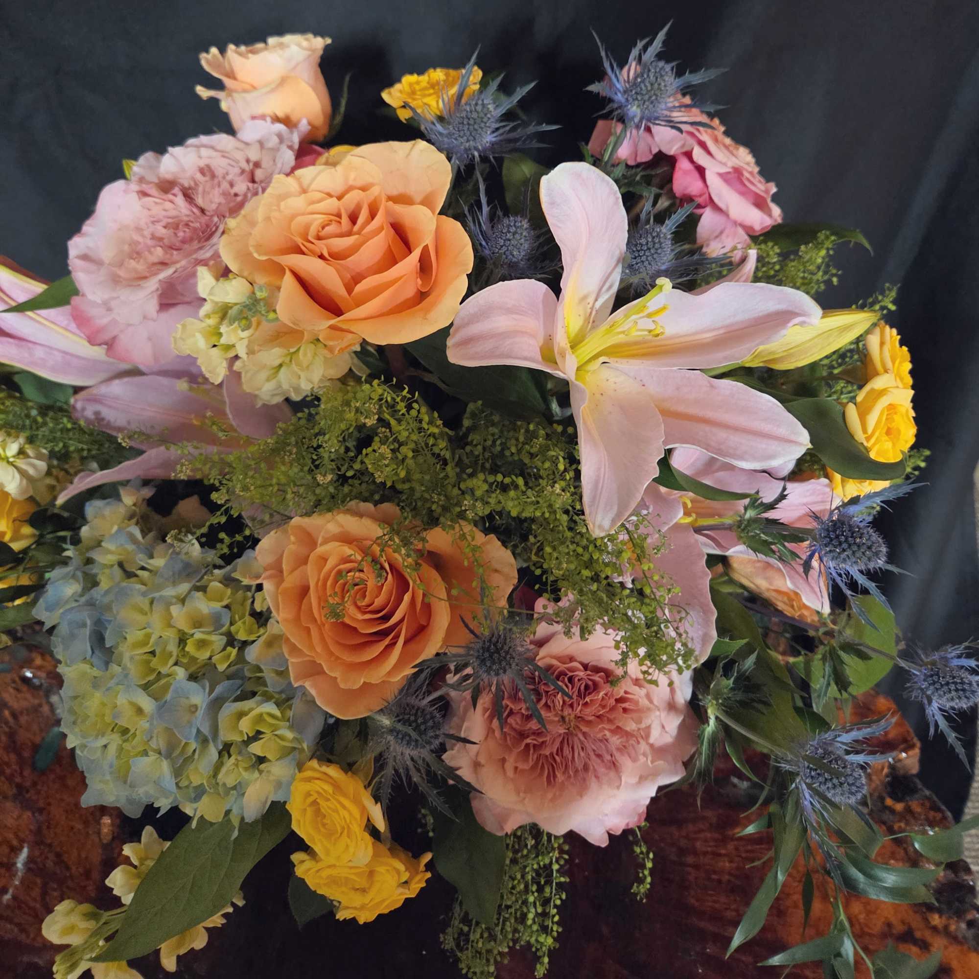 A lush, garden-inspired arrangement overflowing with soft peach and blush blooms, blue