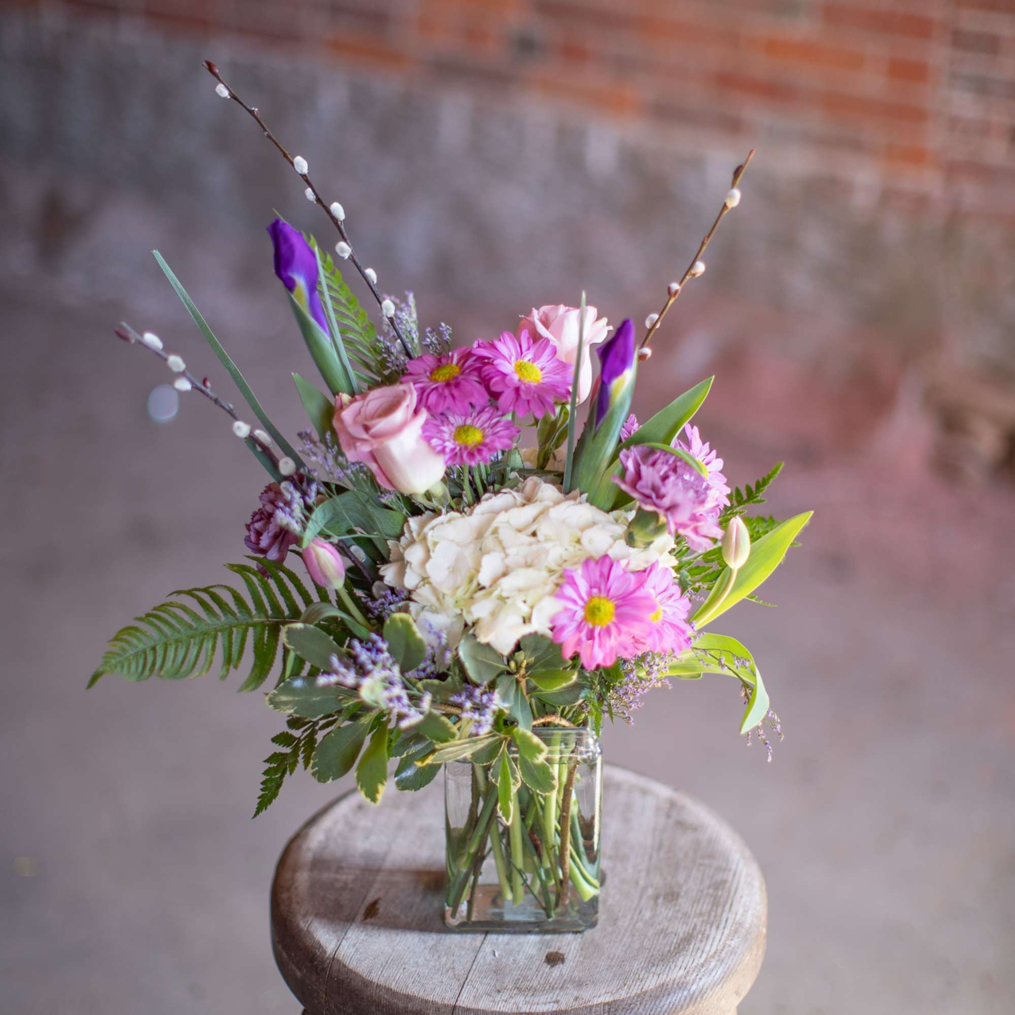 Pink and white flowers in a clear glass vase on a wooden stool