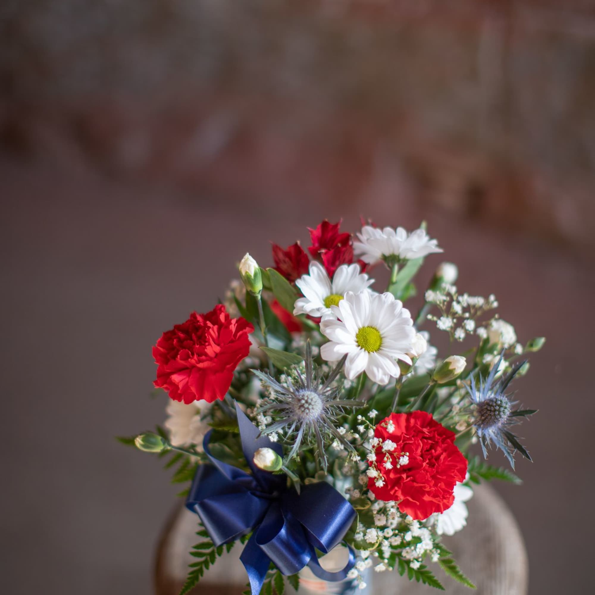 Bouquet of red carnations and white daisies in a glass vase with a blue ribbon