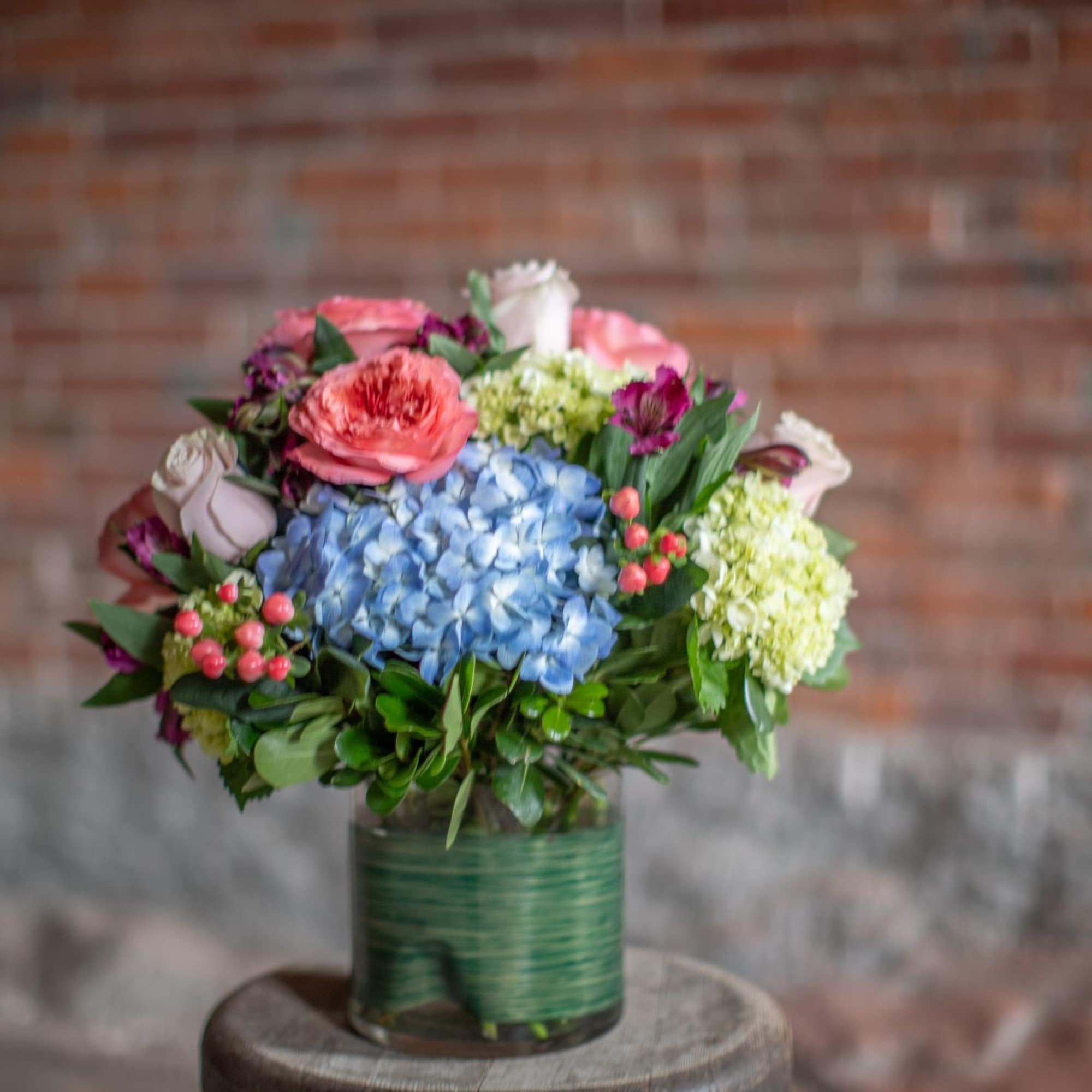 Mixed bouquet in a green glass vase with blue hydrangea and pink roses