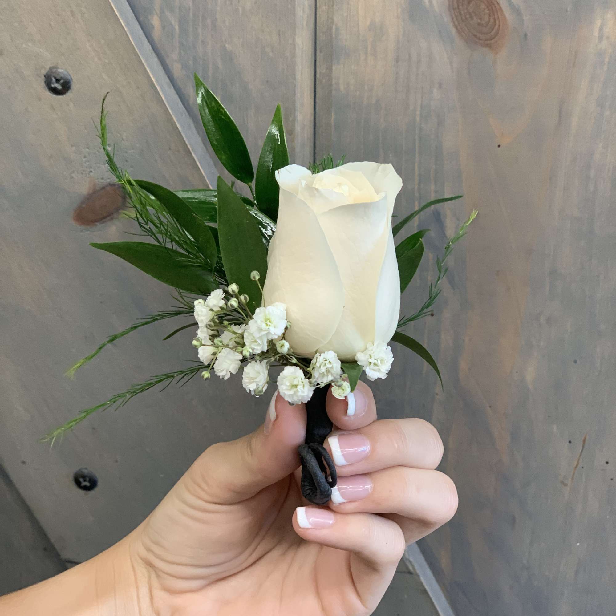 White rose boutonniere with small white filler flowers and greenery