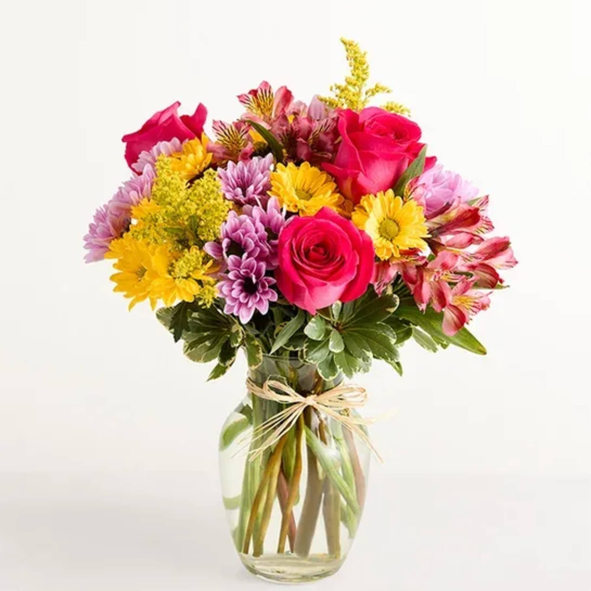 Bright mixed bouquet of pink roses, yellow and purple daisies in a clear glass vase with twine bow