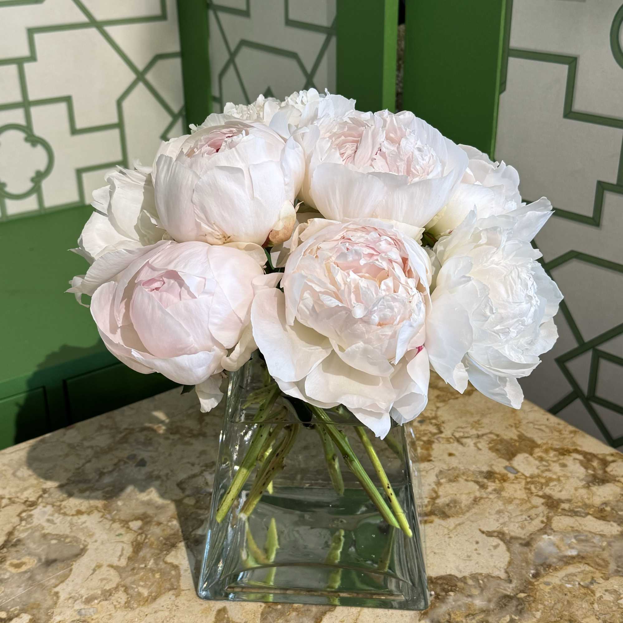 White and pale pink peonies arranged in a clear glass vase