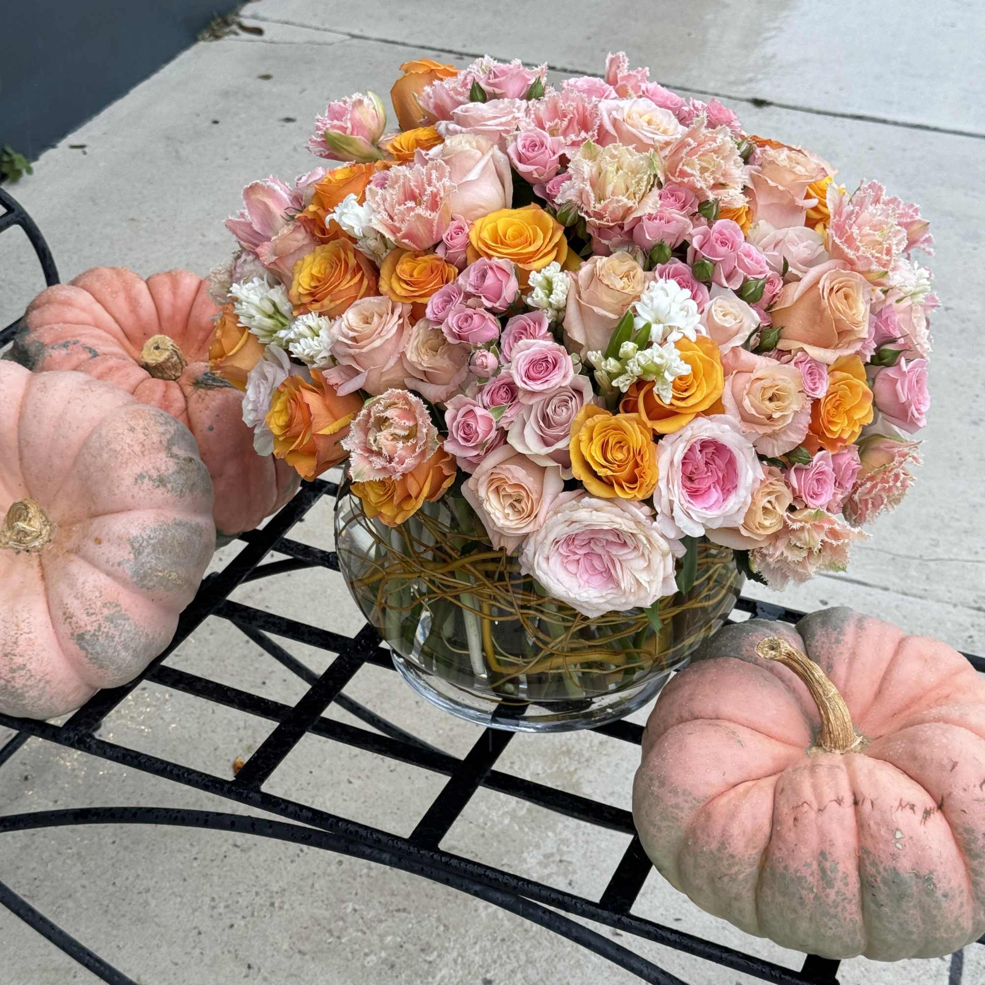 Pink and orange rose bouquet in a glass vase with pumpkins nearby