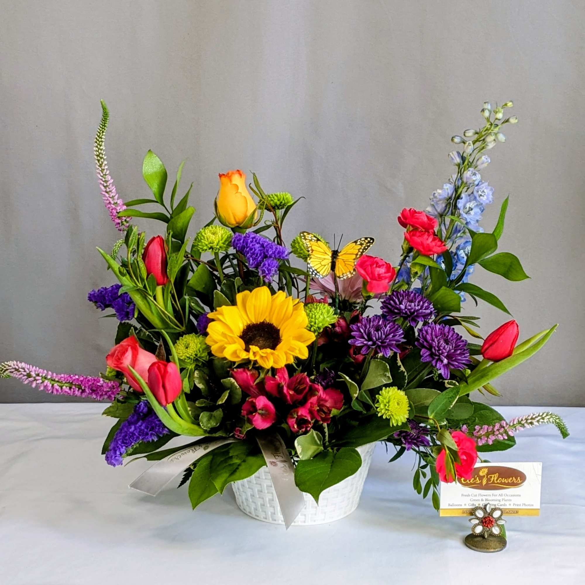 Colorful mixed flower arrangement in a white basket with a butterfly pick