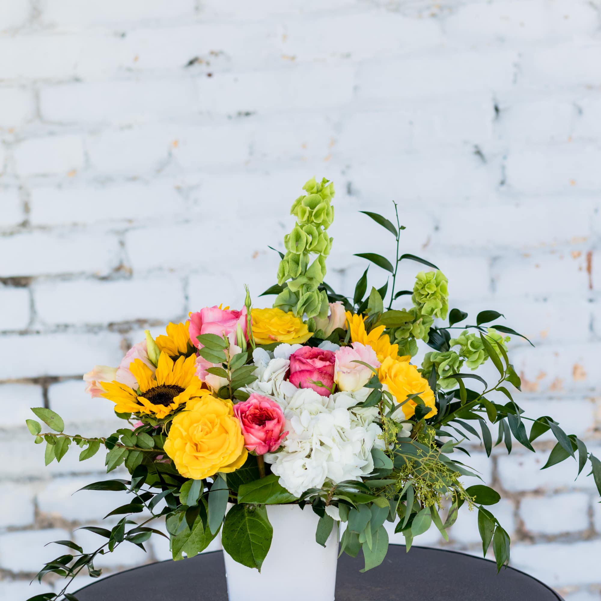Mixed bouquet in a white container with yellow, pink, and white flowers