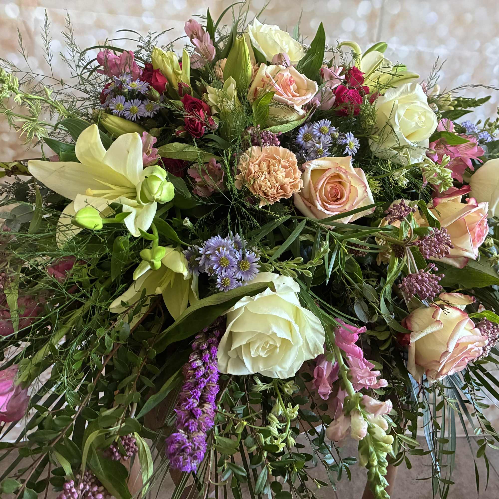 Mixed bouquet of roses, lilies, and small purple flowers in soft pink and white.