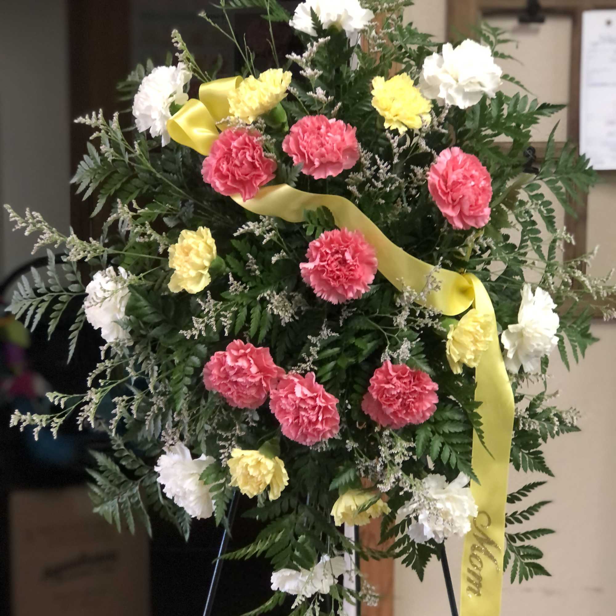 Standing floral spray with pink, white, and yellow carnations on a ribboned easel