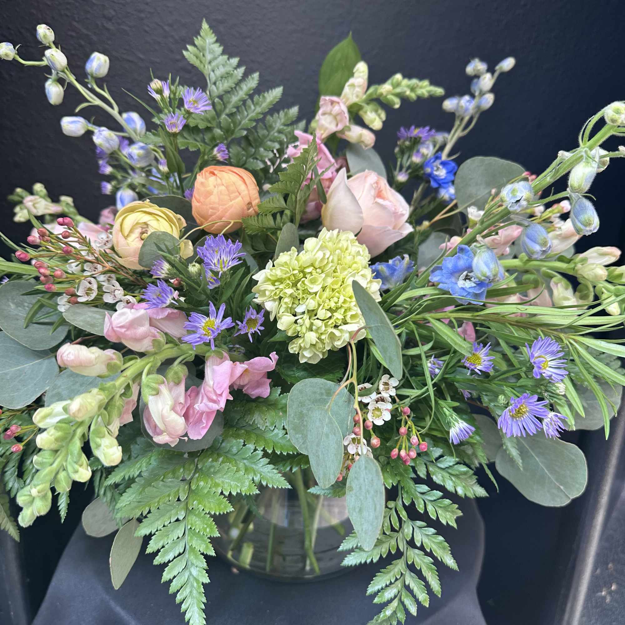 Pastel mixed flower arrangement with roses, ranunculus, and snapdragons in a clear glass vase