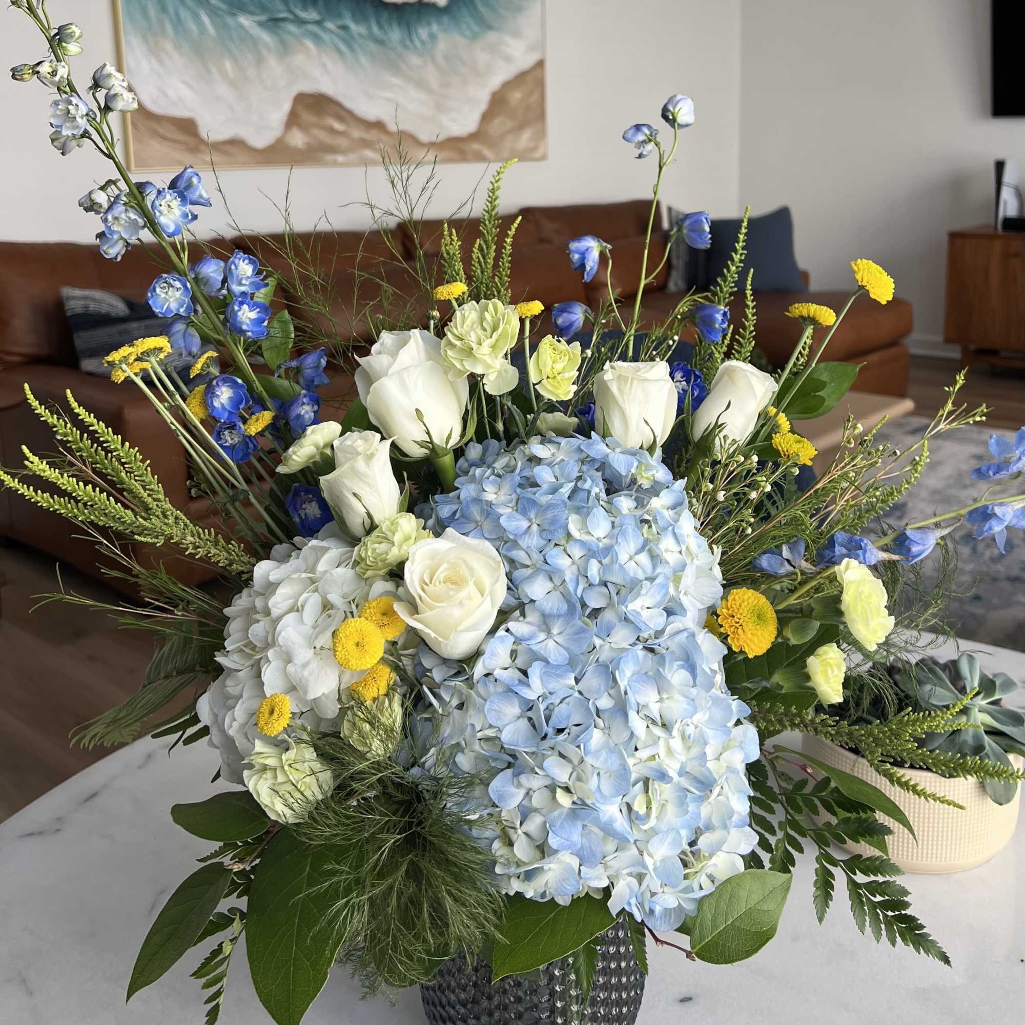 Blue and white floral arrangement with roses, hydrangeas, and yellow accents in a vase