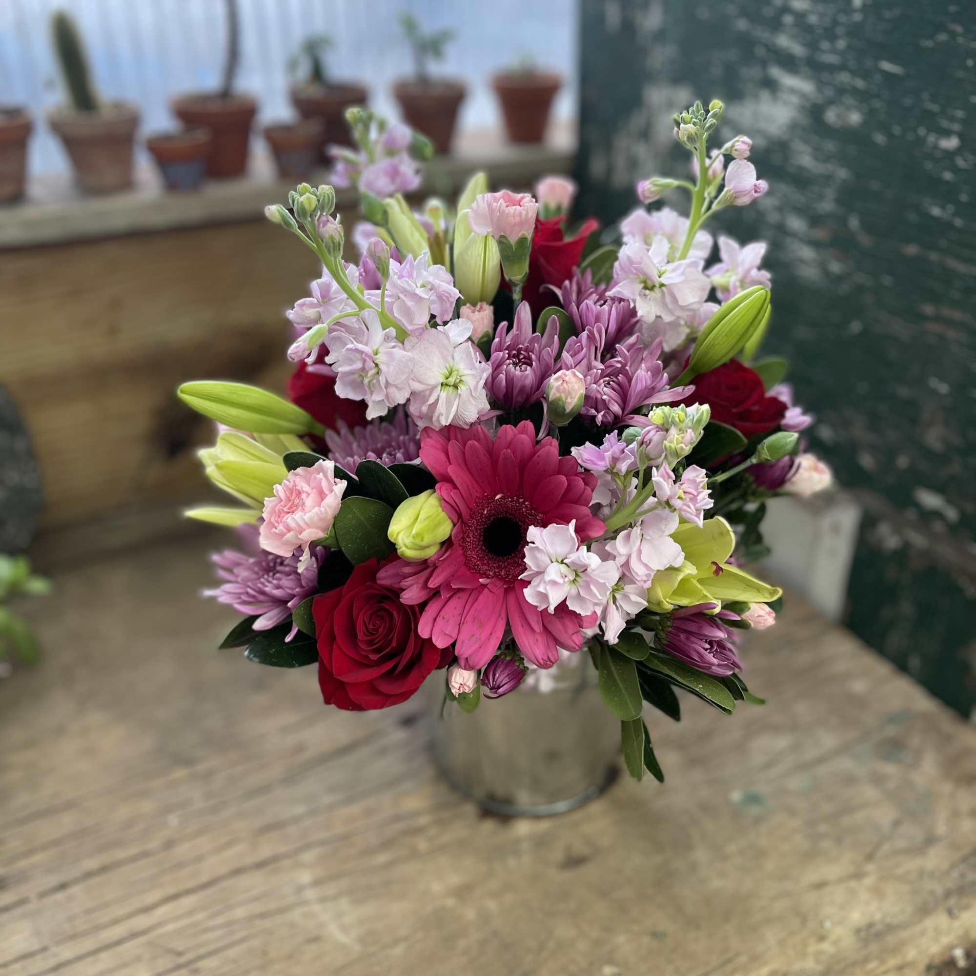 Mixed bouquet with pink gerbera, red roses, and lilies in a metal vase