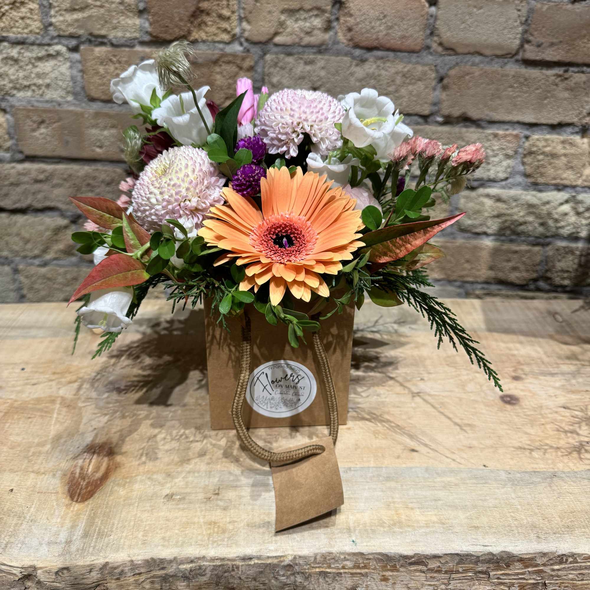 Mixed bouquet with an orange gerbera daisy in a brown gift bag