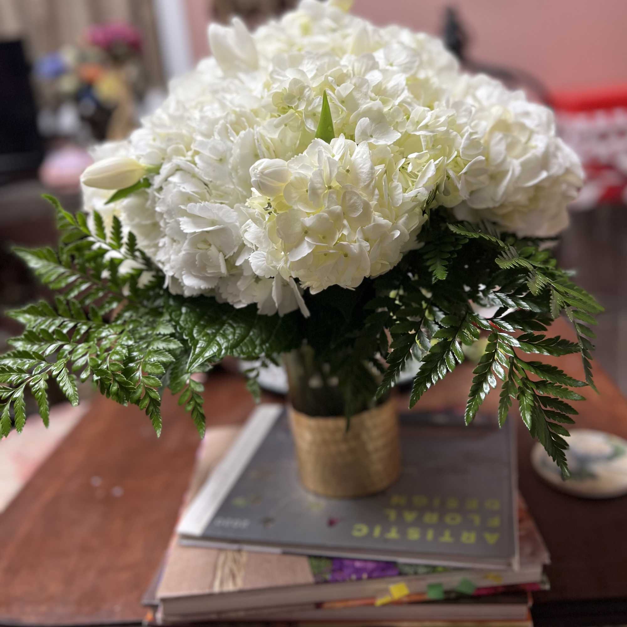 White hydrangea bouquet in a gold wrap vase with fern foliage