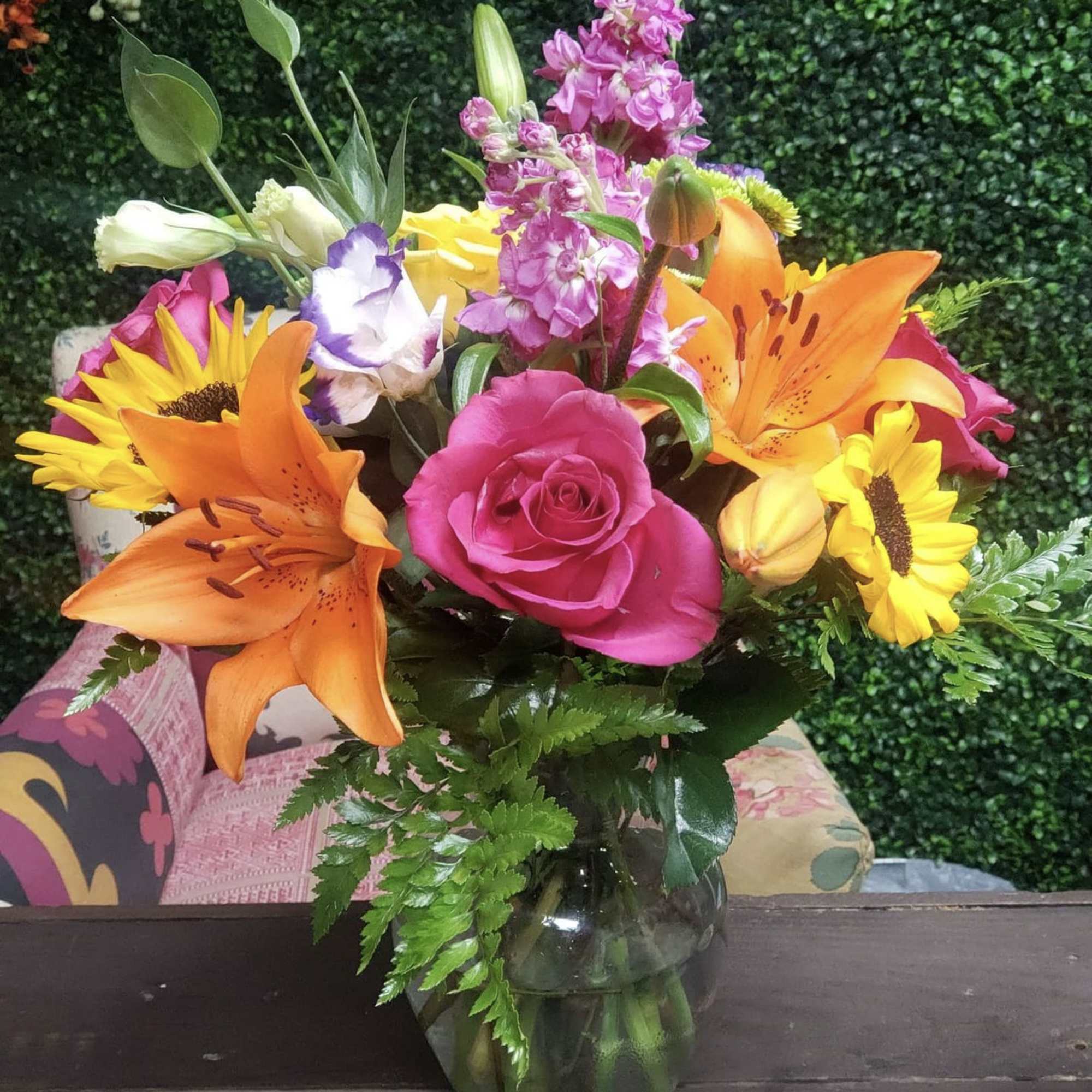 Mixed bouquet of pink roses, orange lilies, and sunflowers in a glass vase