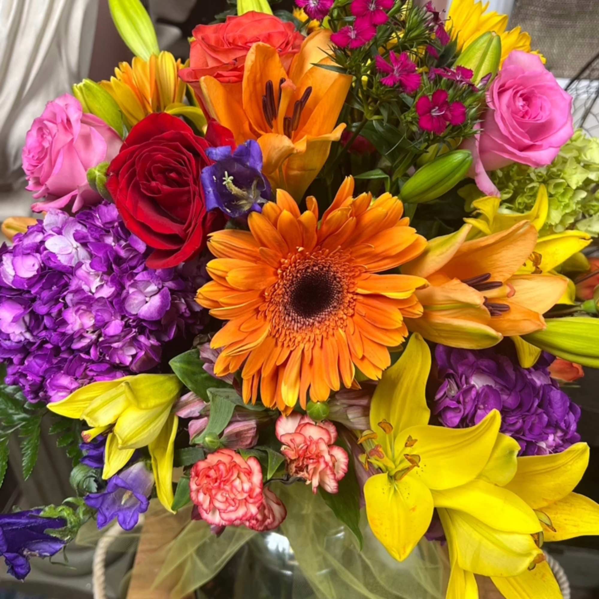 Colorful mixed bouquet with roses, lilies, gerbera daisies, and purple hydrangeas in a glass vase