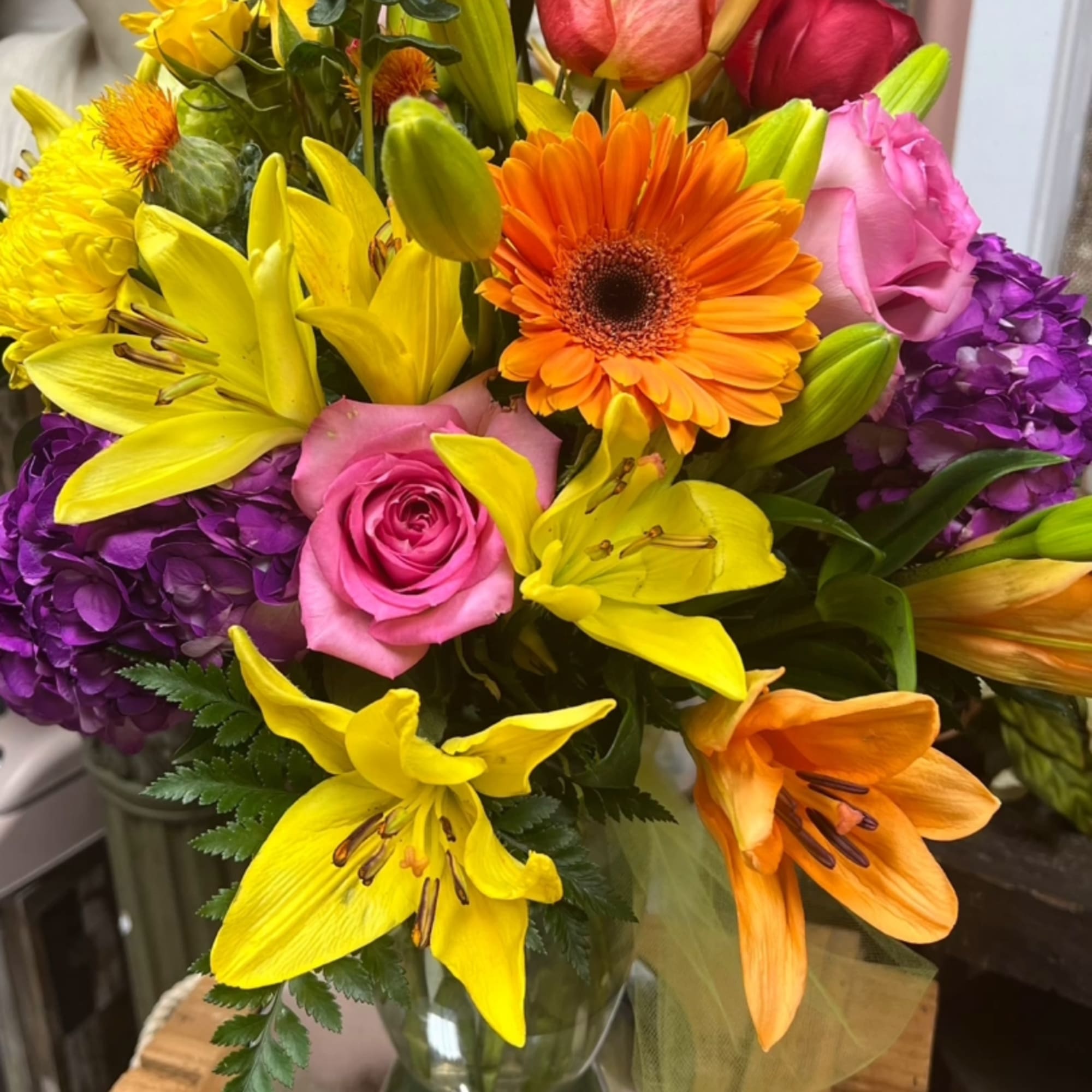 Mixed bouquet of roses, lilies, gerbera daisies, and hydrangeas in a glass vase