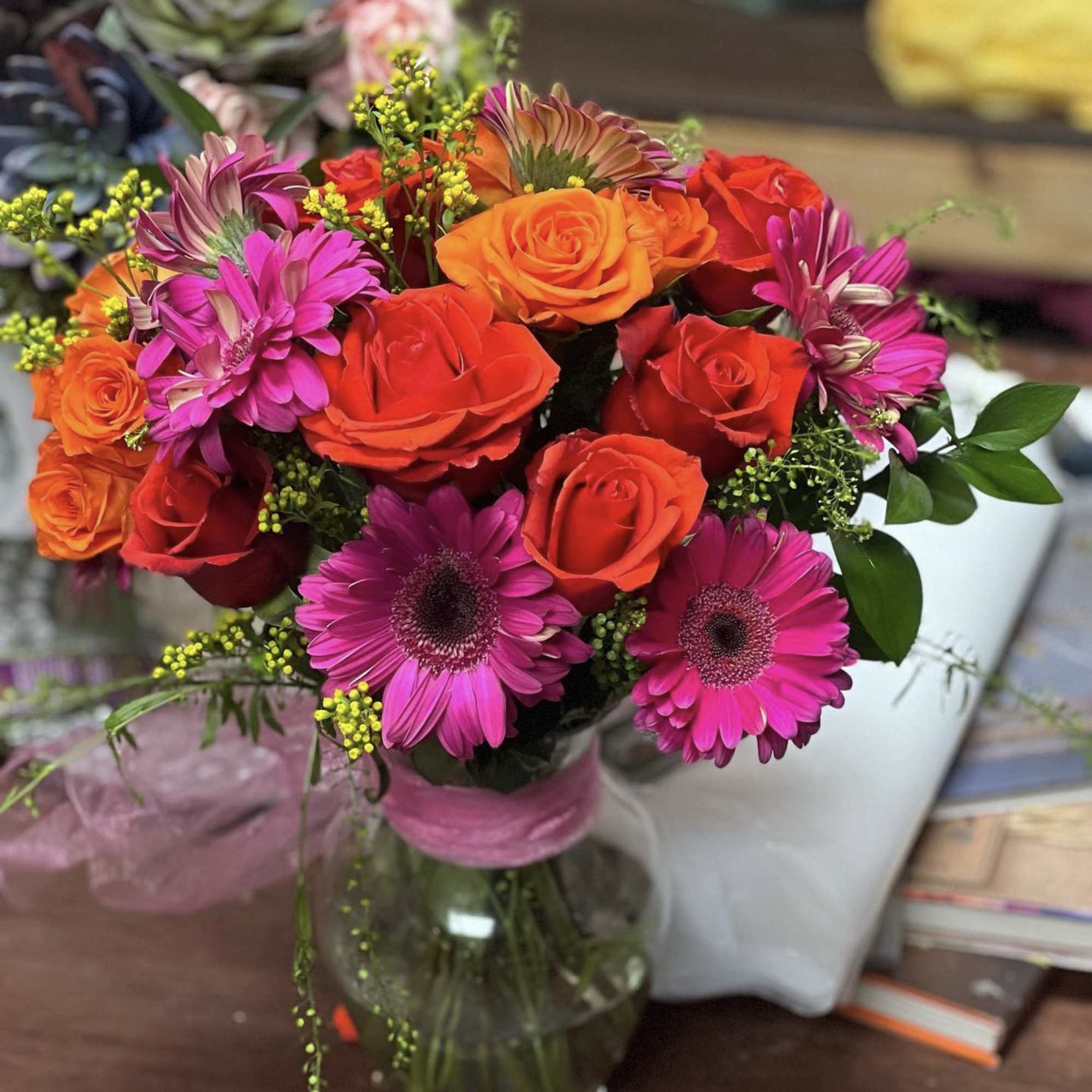 Bouquet of orange and red roses with pink daisies in a glass vase