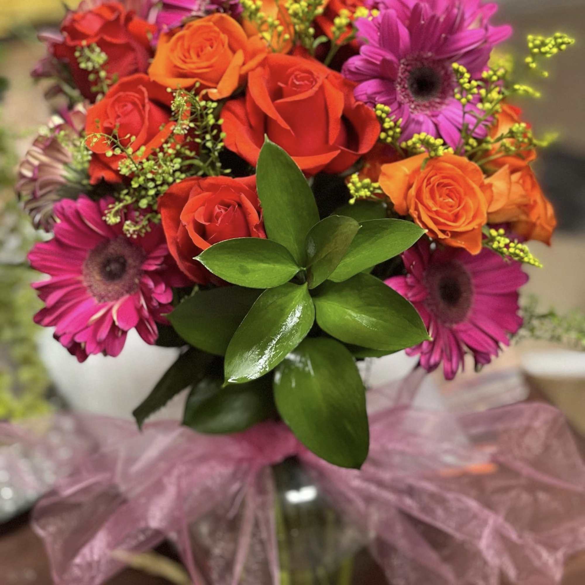 Bouquet of red and orange roses with pink gerbera daisies in a glass vase