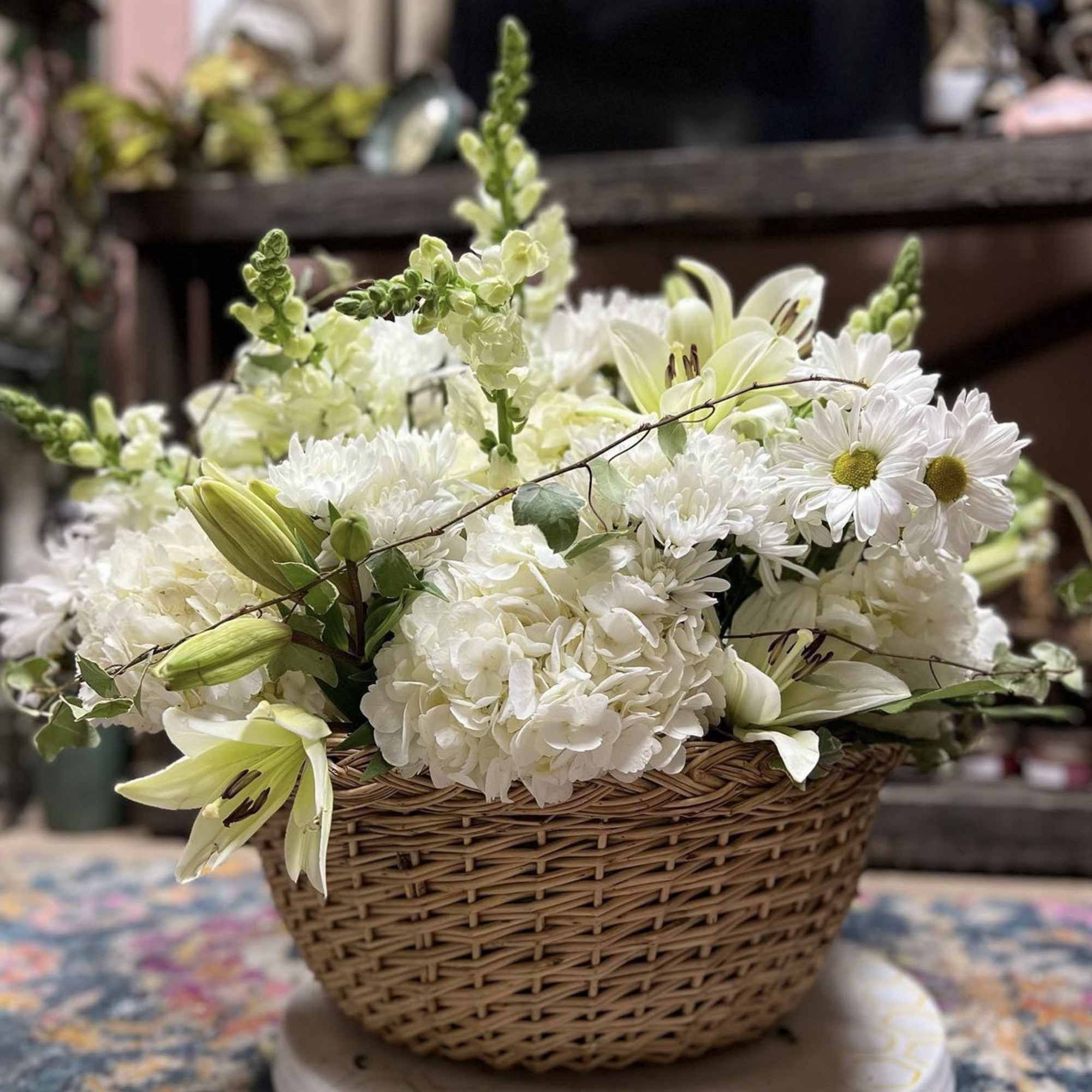 White flowers arranged in a wicker basket with pale lilies and daisies