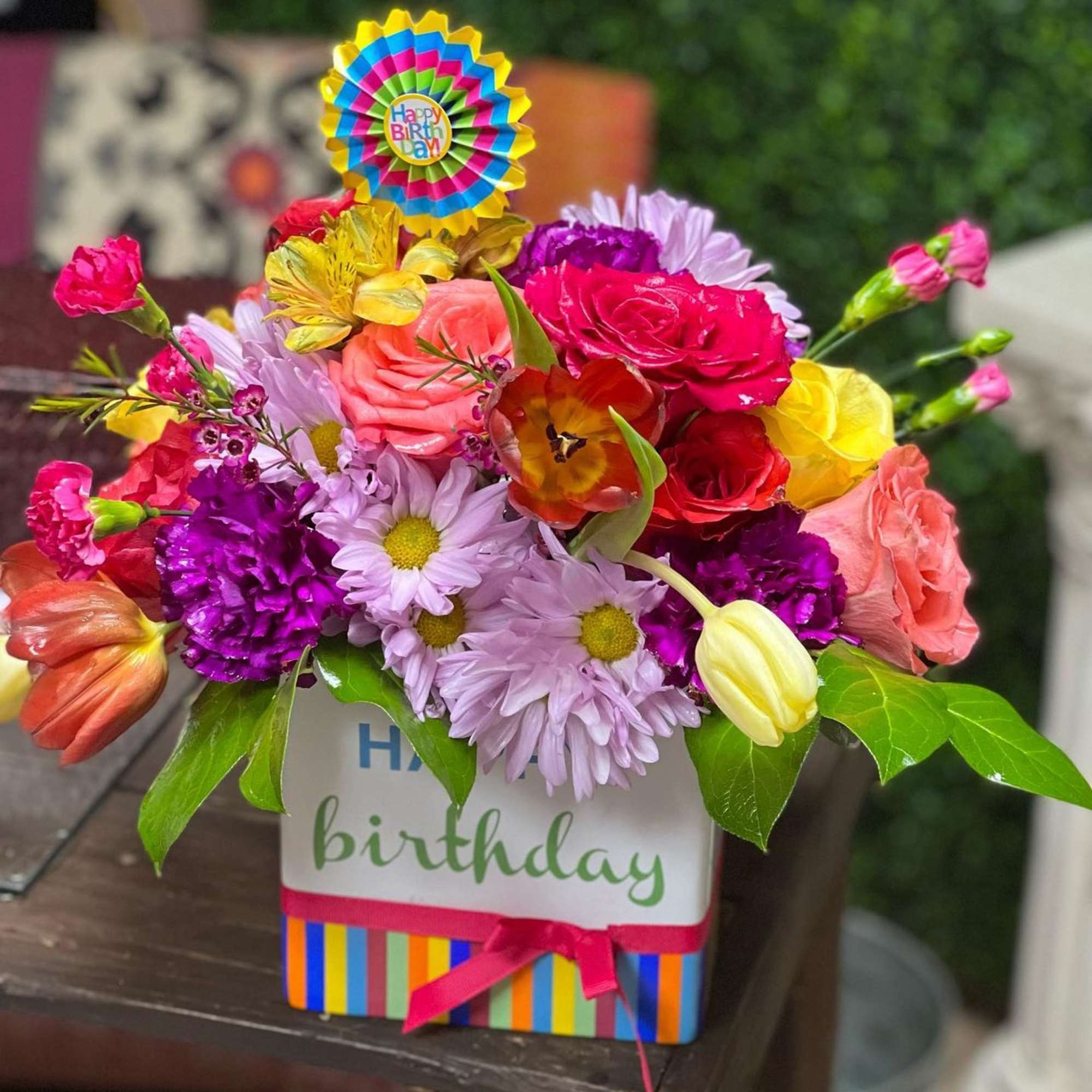 Colorful birthday flower arrangement in a striped gift box with a topper