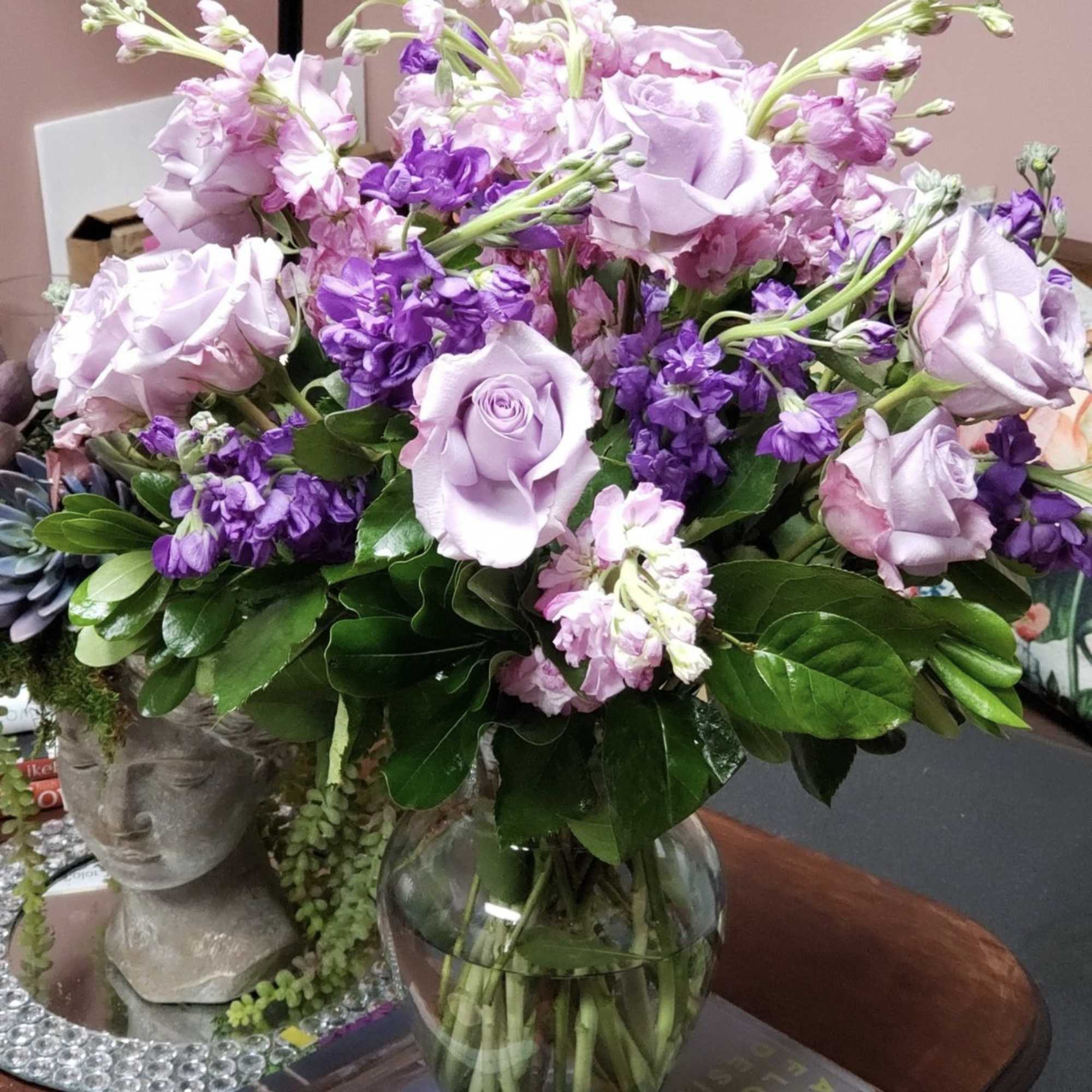 Lavender roses and purple flowers arranged in a glass vase