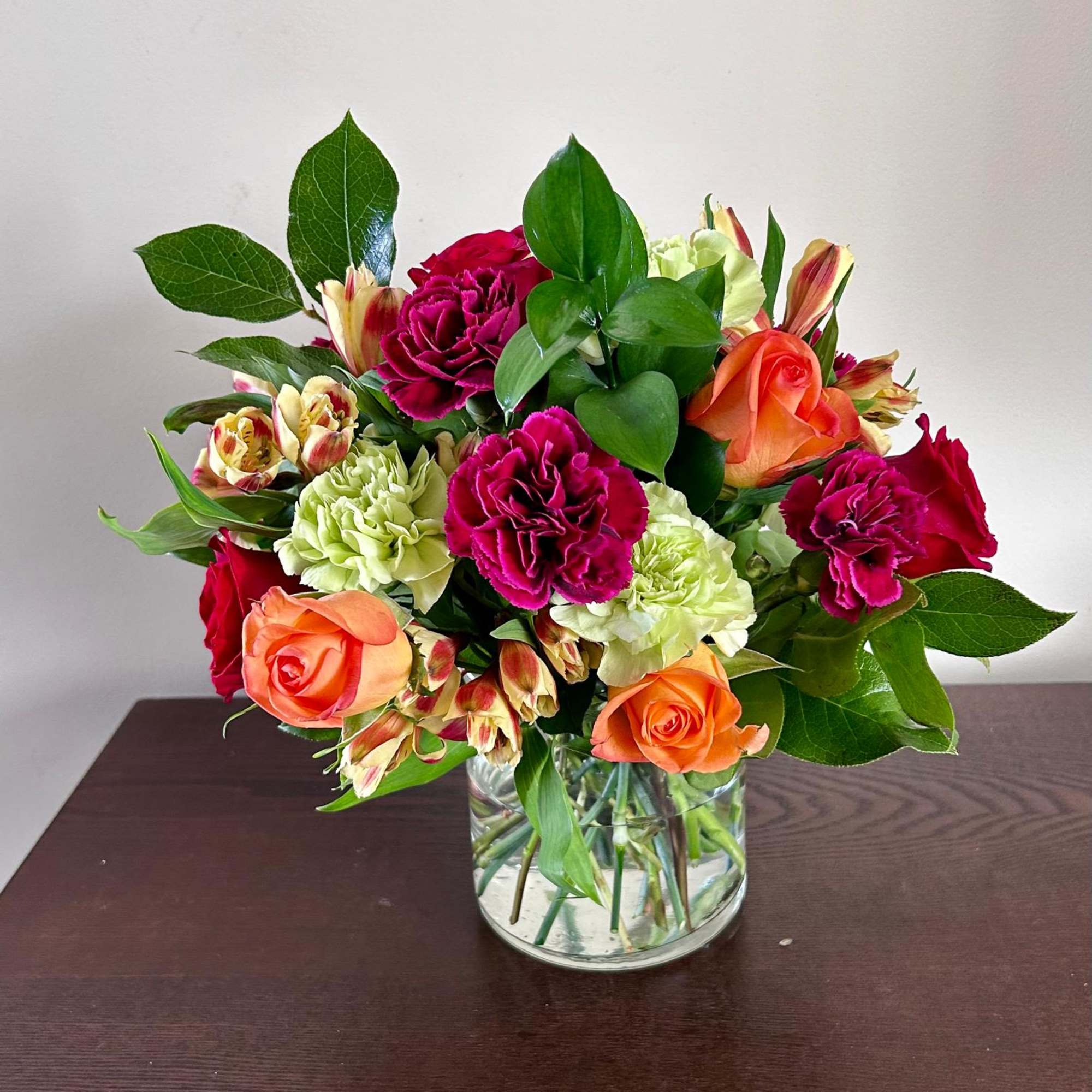 Mixed bouquet of roses, carnations, and alstroemeria in a clear glass vase