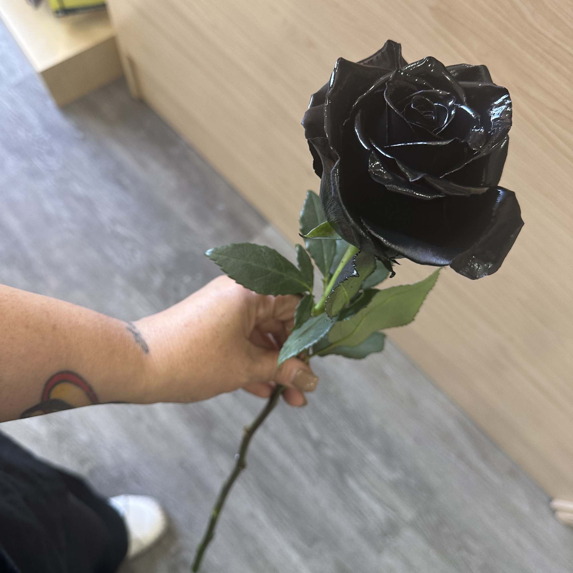 Long stem black roses arranged in a tall vase with greens and