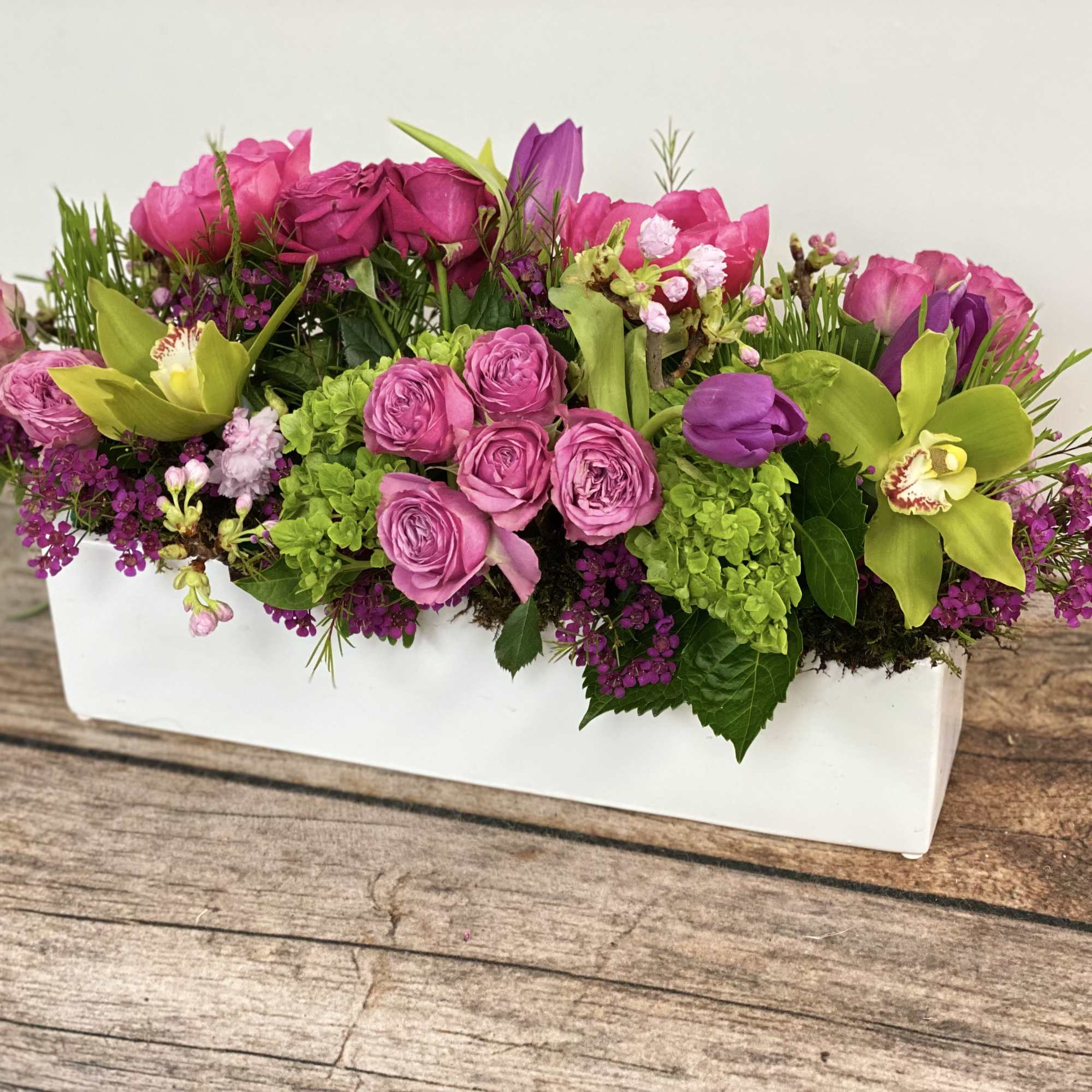 Pink and purple floral arrangement in a white rectangular vase
