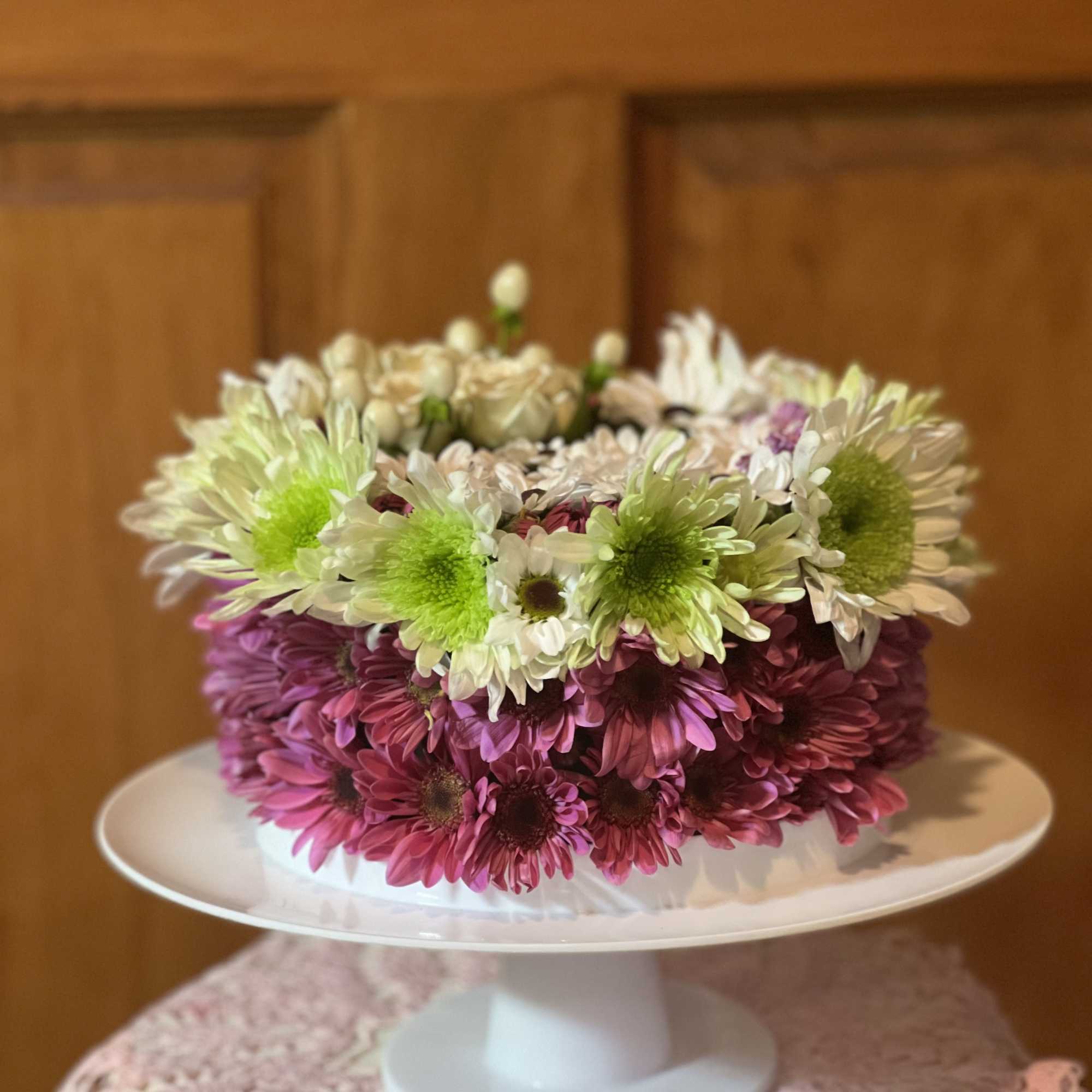Round arrangement of pink and white daisies on a white pedestal stand