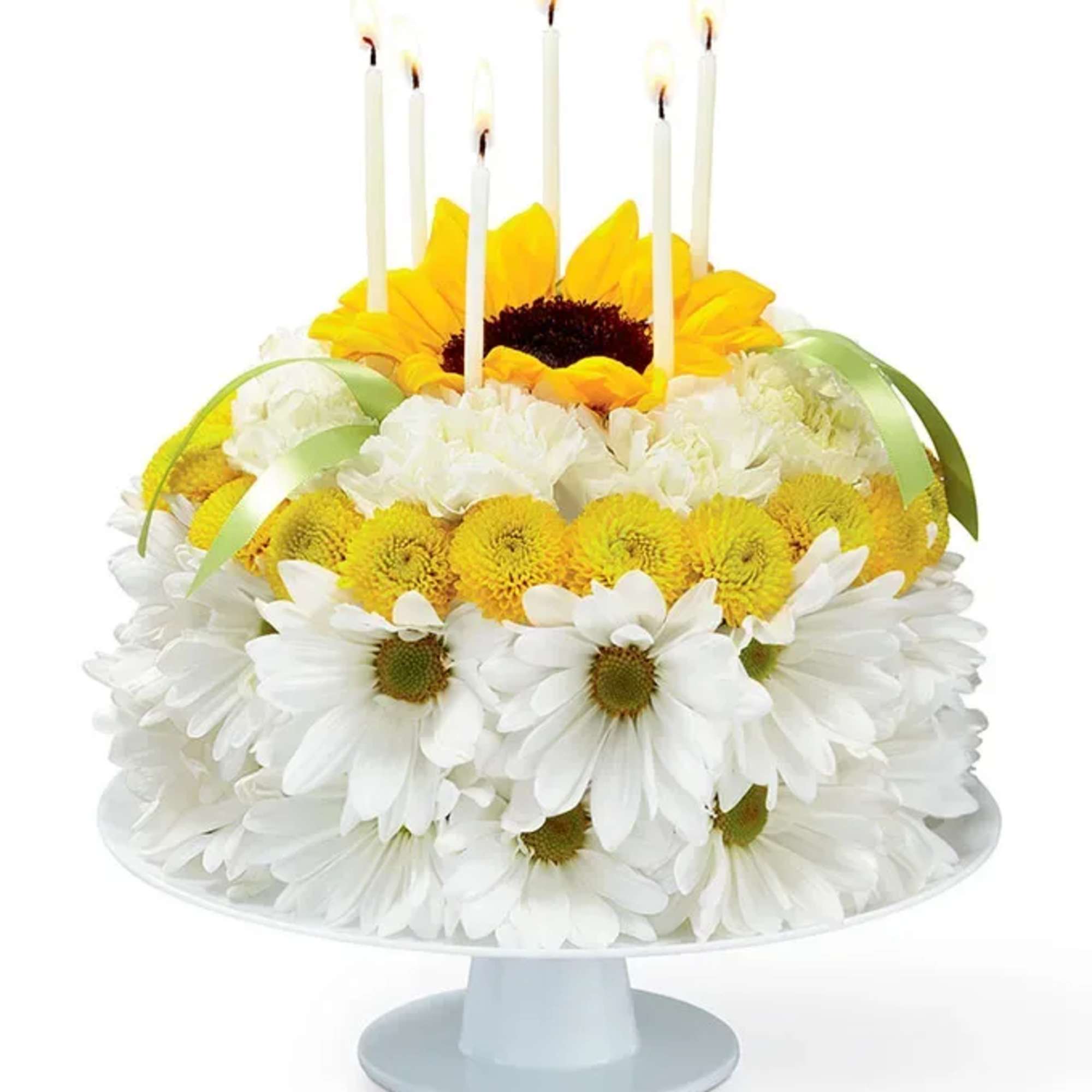 White and yellow daisy cake with lit candles on a pedestal stand