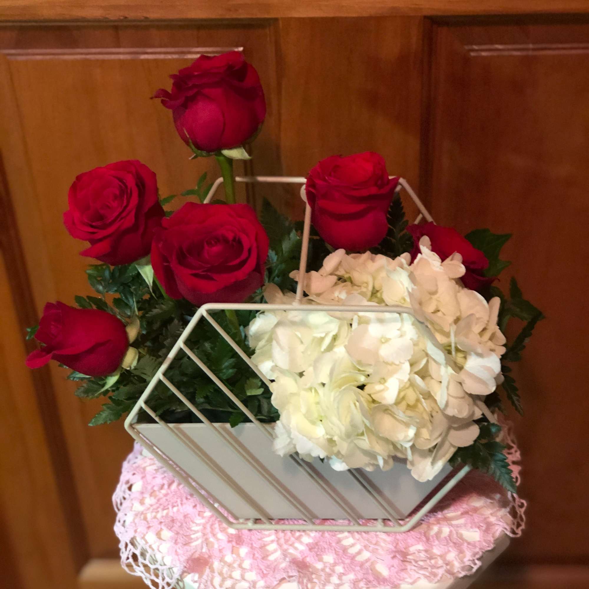 Red roses and white hydrangeas arranged in a white basket-style container