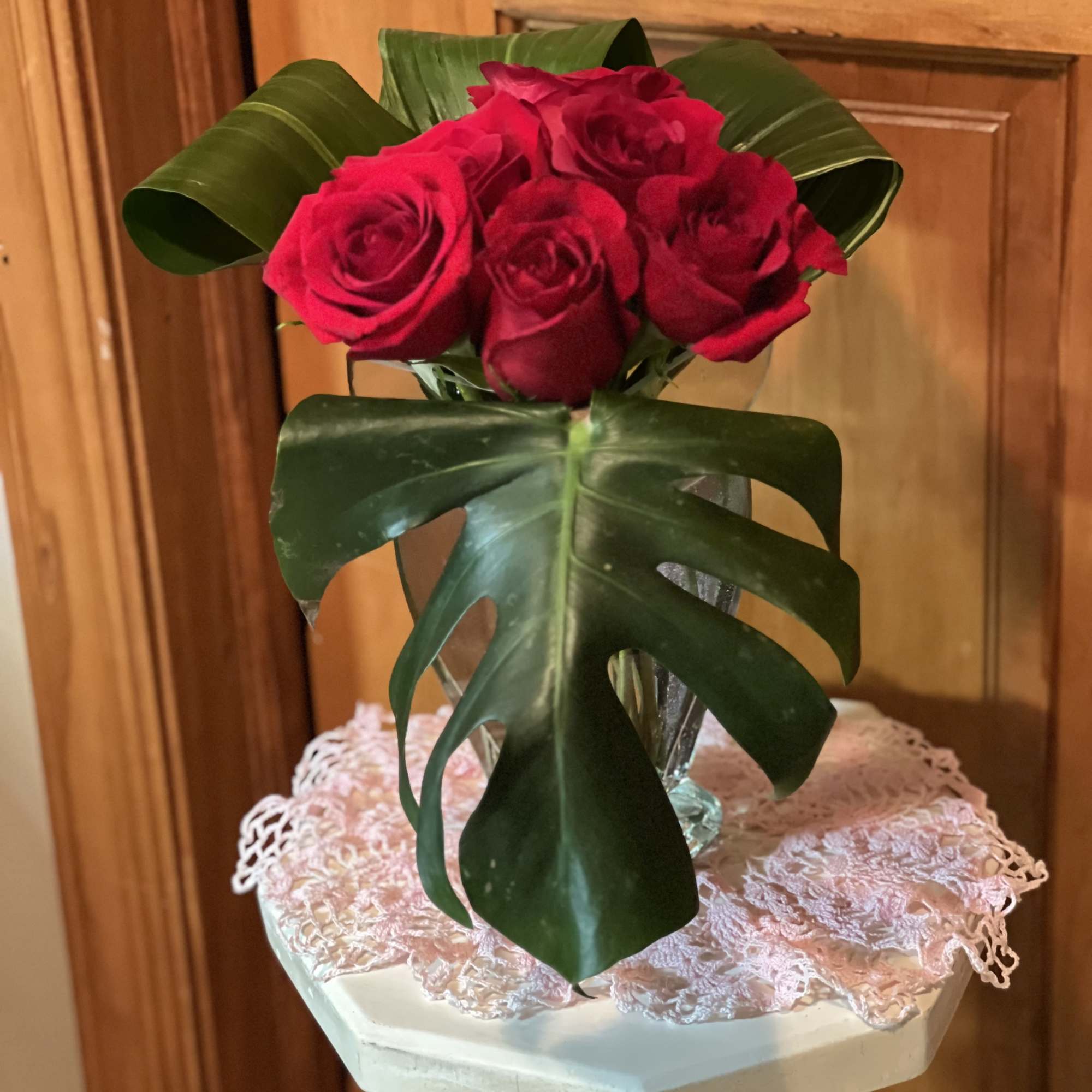 Small bouquet of red roses in a clear vase with large tropical leaves