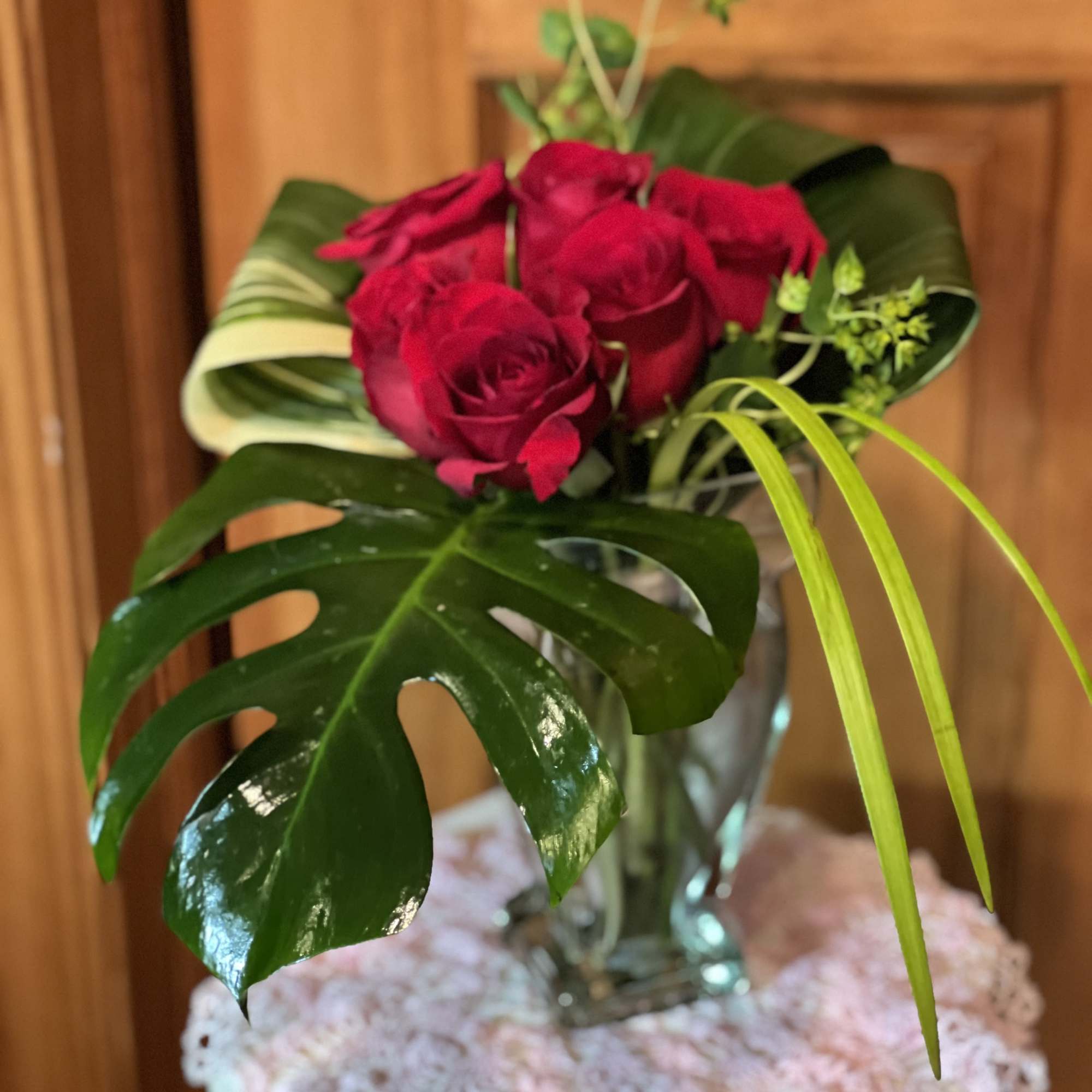 Red roses in a clear glass vase with large tropical leaves