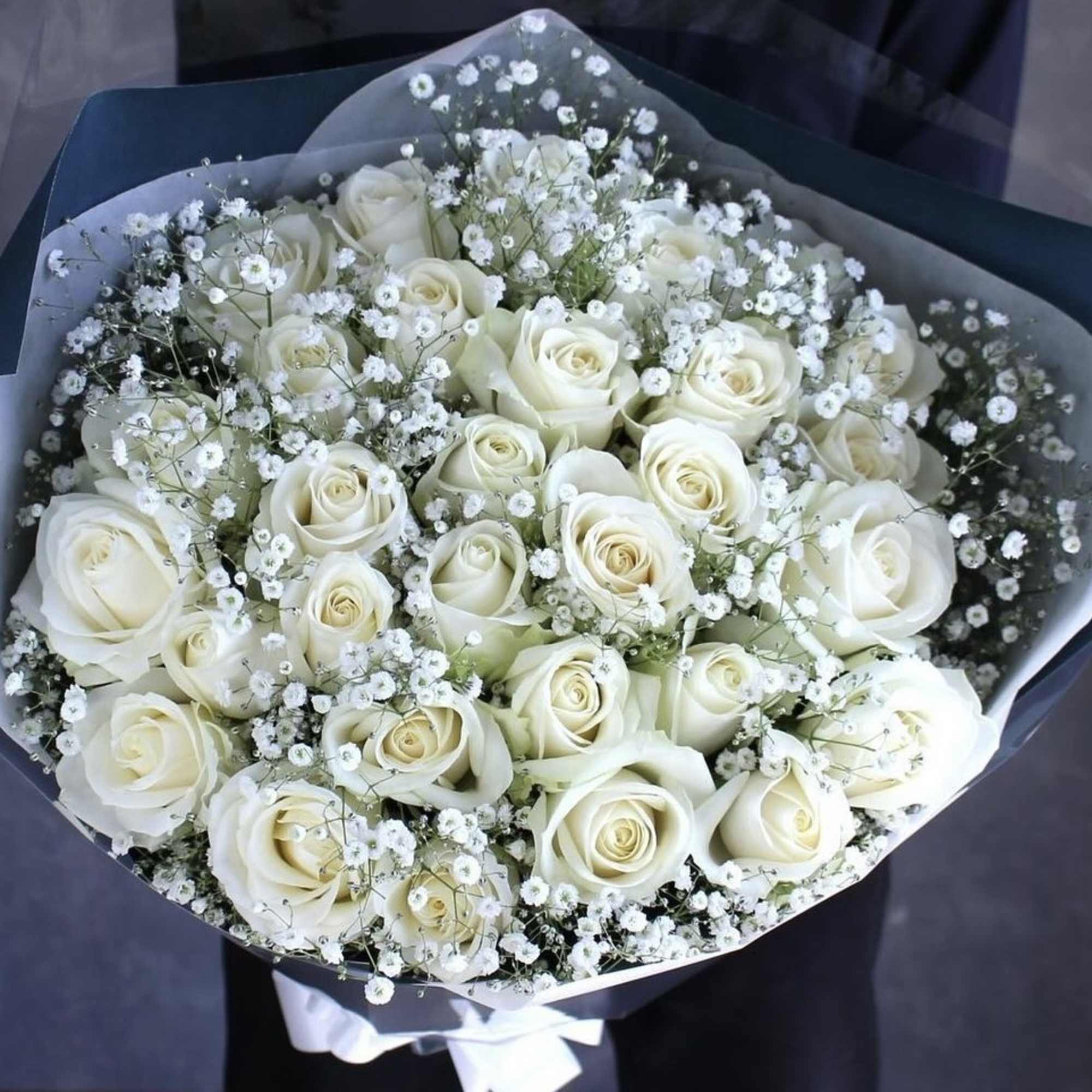 Bouquet of white roses and baby's breath wrapped in dark paper