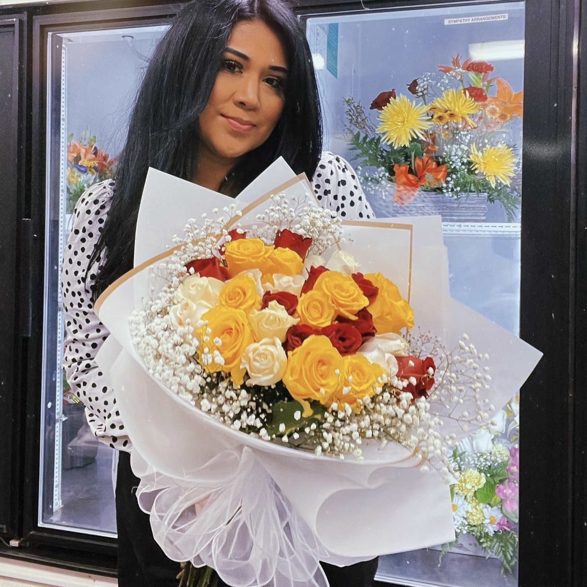 Woman holding a bouquet of yellow, red, and white roses wrapped in white paper