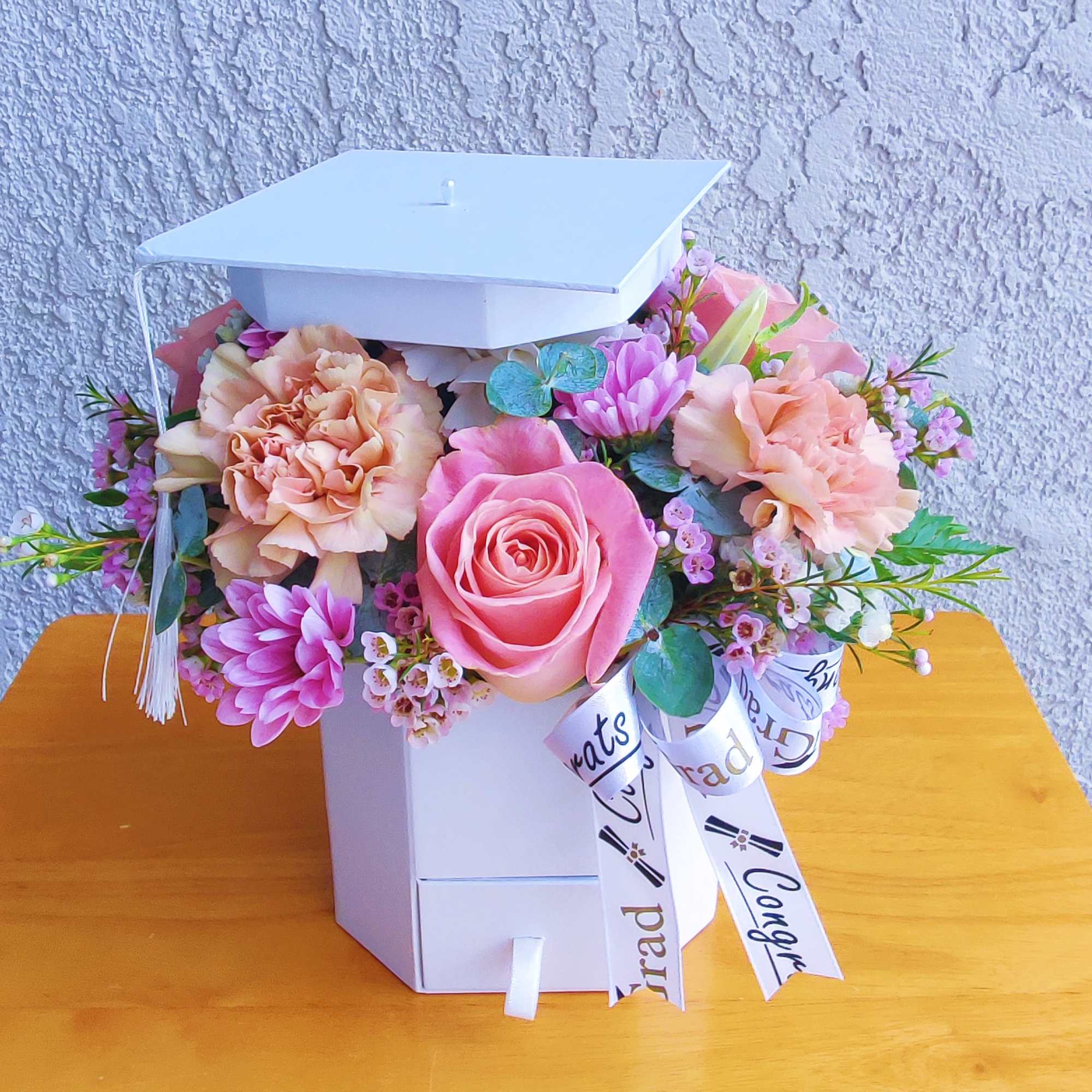 Pink and peach flowers arranged in a white graduation box with a cap lid