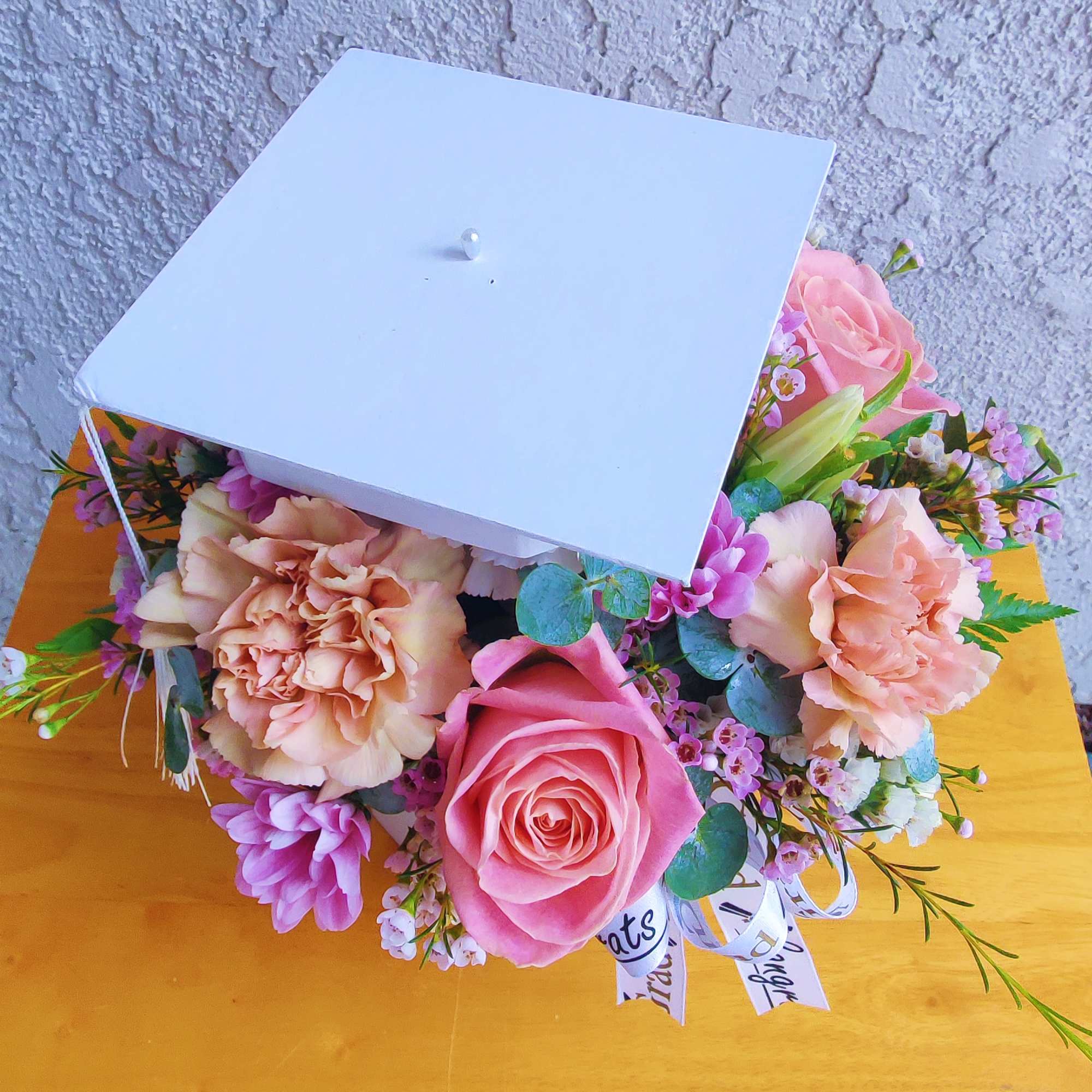 Pink and peach flowers arranged in a white gift box with a lid