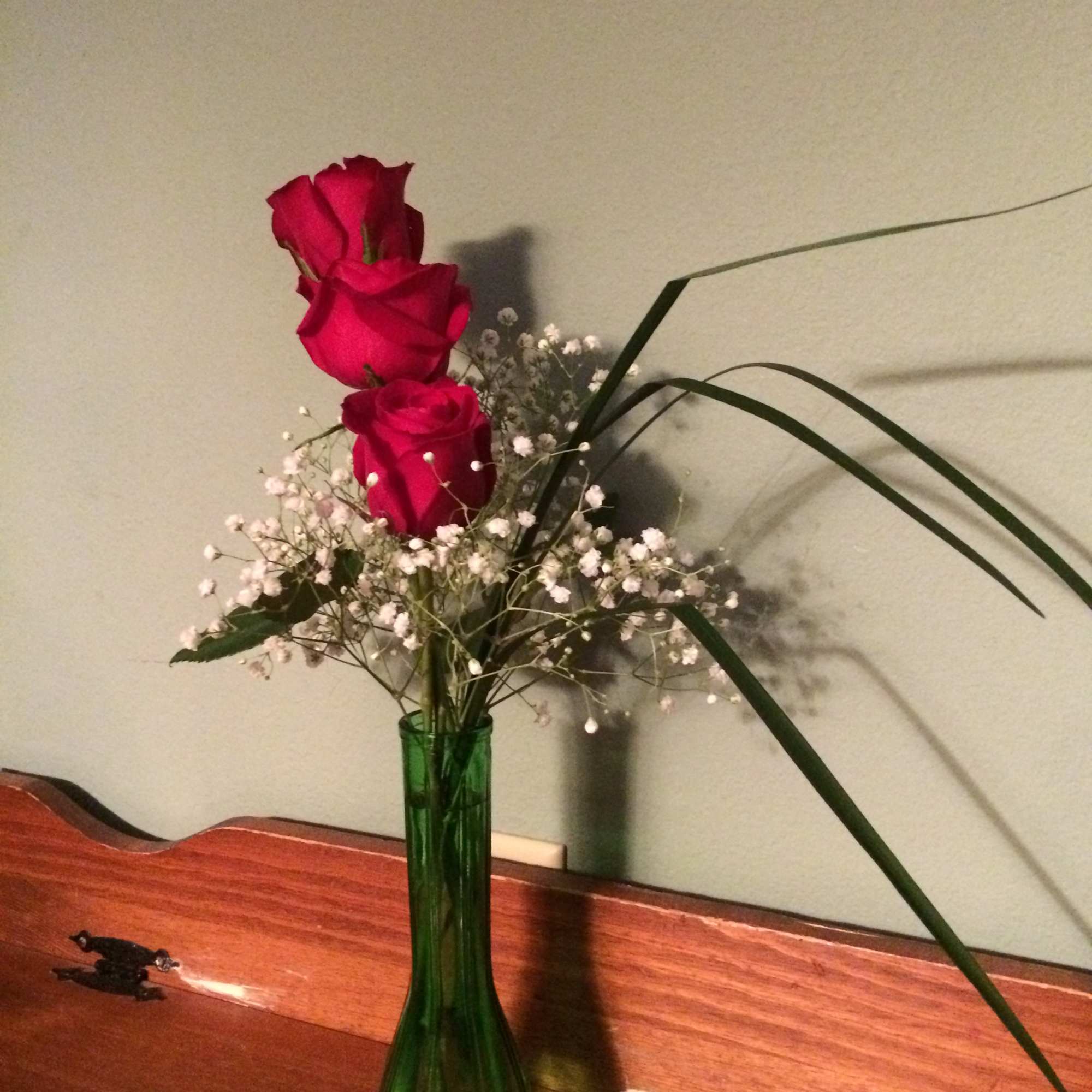 Three red roses in a green glass vase with baby's breath
