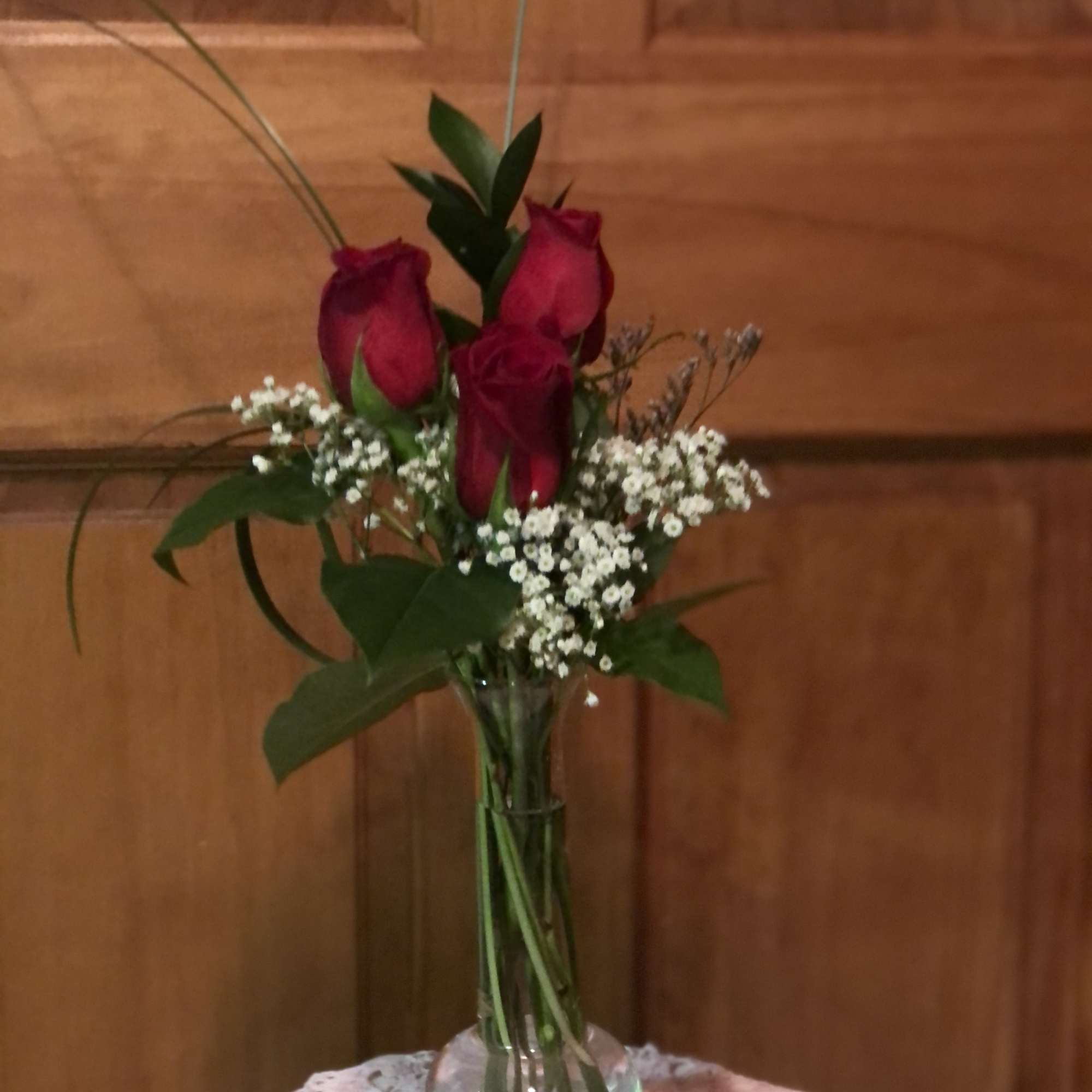 Three red roses in a clear glass vase with baby's breath