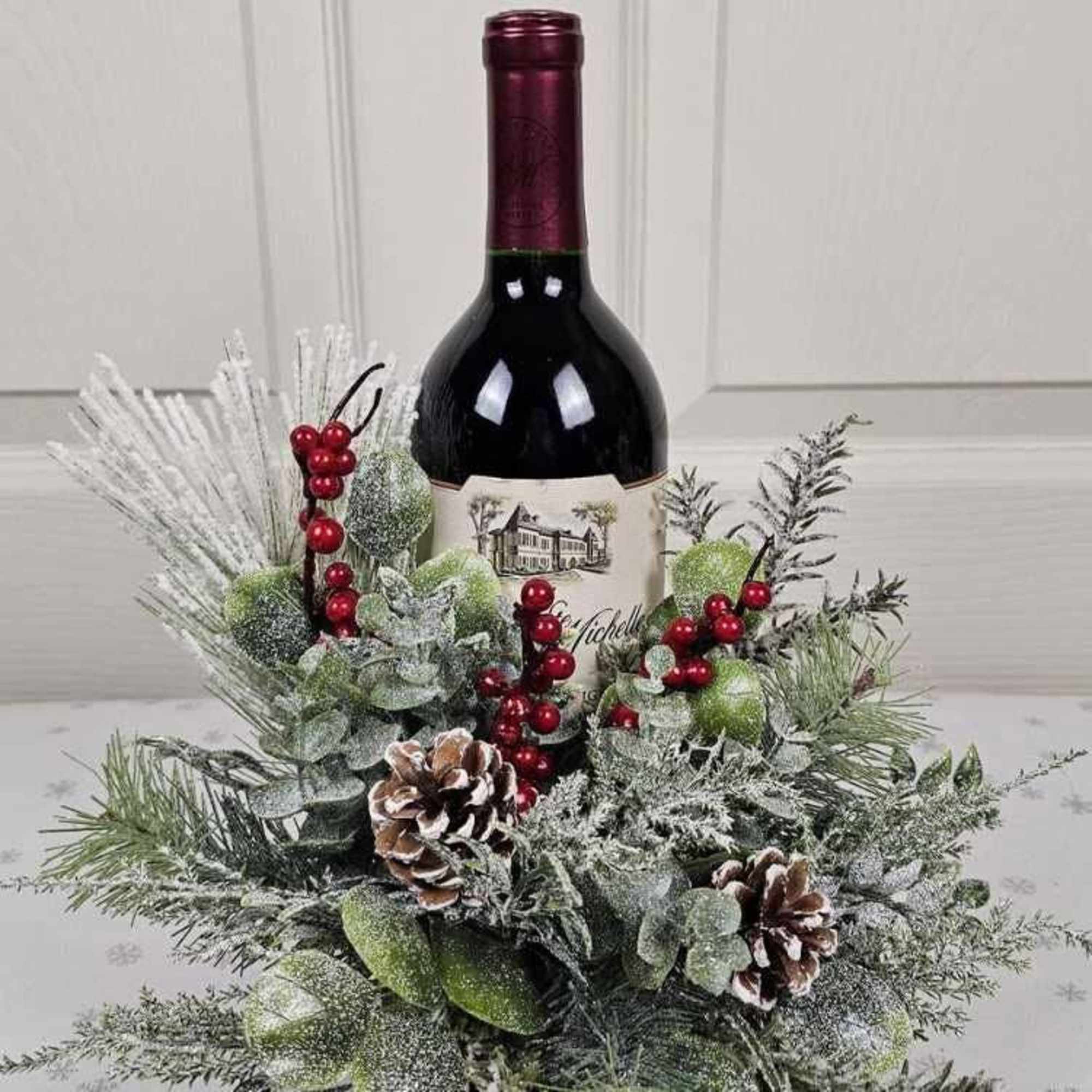 Wine bottle arranged with frosted greenery, red berries, and pinecones